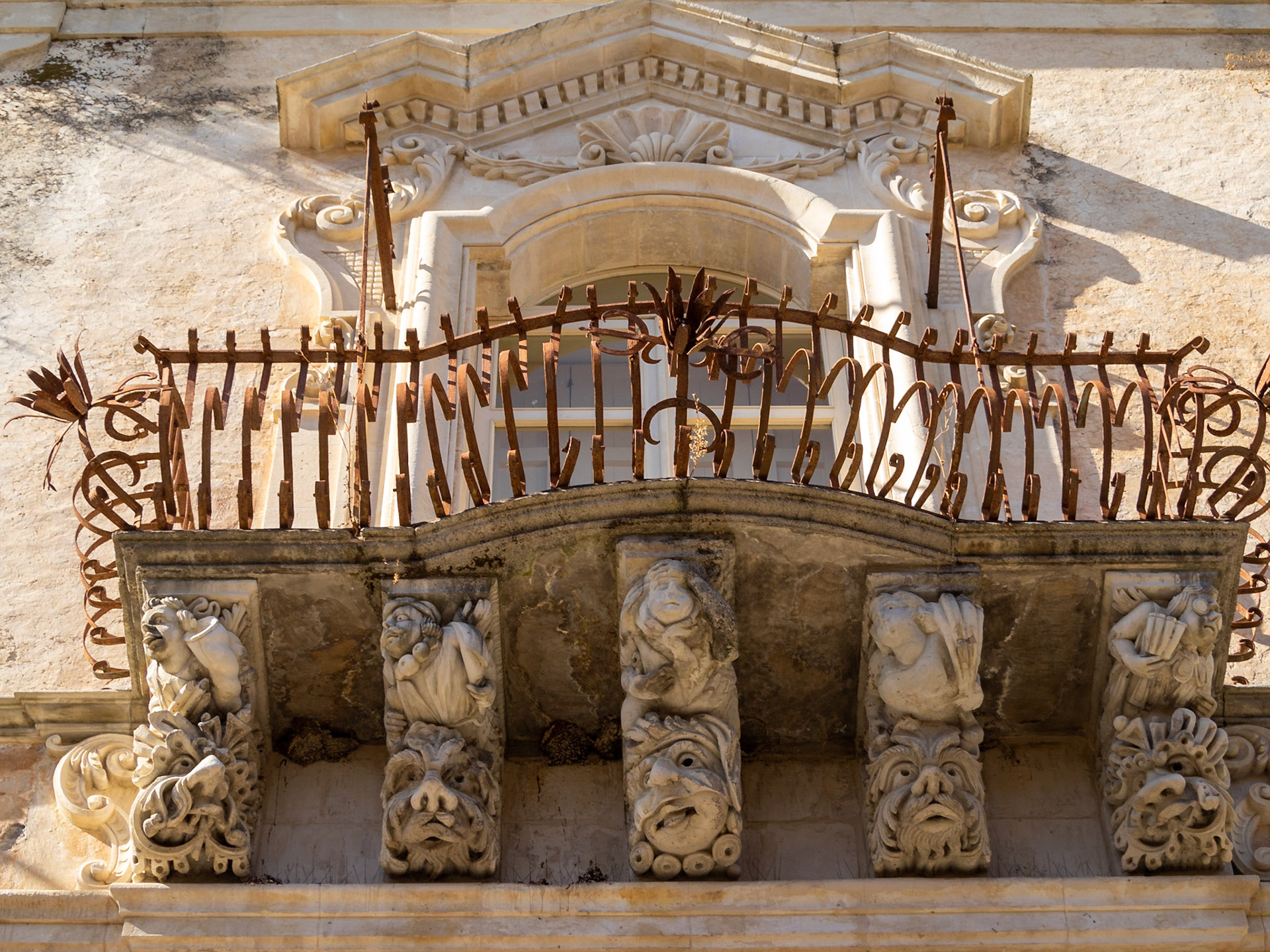 Looking up at the stone carved faces supporting a balcony of the baroque Palazzo Cosentini, Ragusa