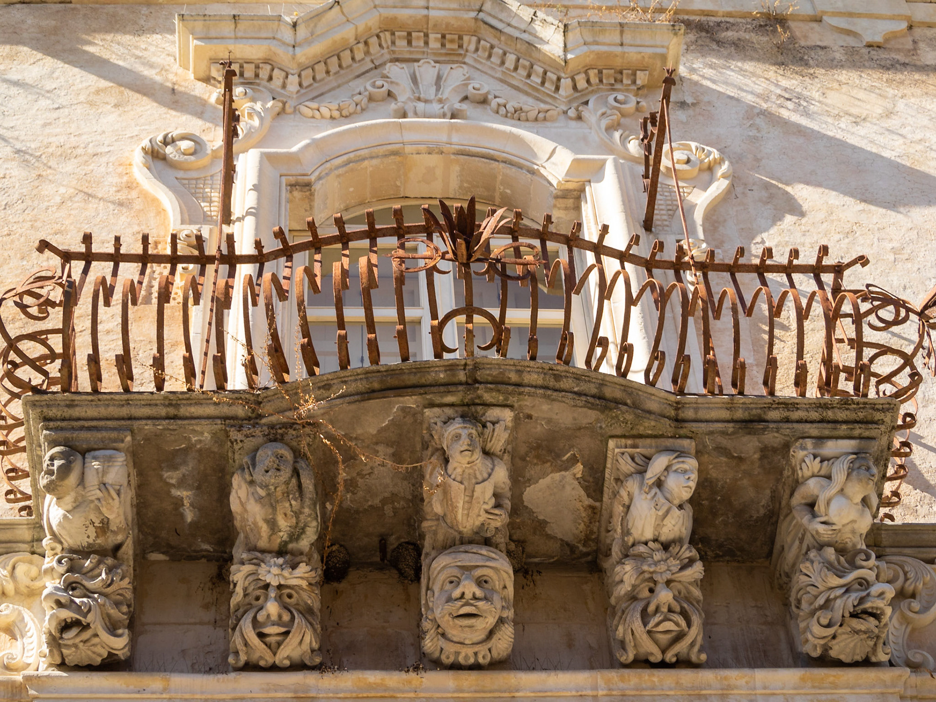 Looking up at the stone carved faces supporting a balcony of the baroque Palazzo Cosentini, Ragusa