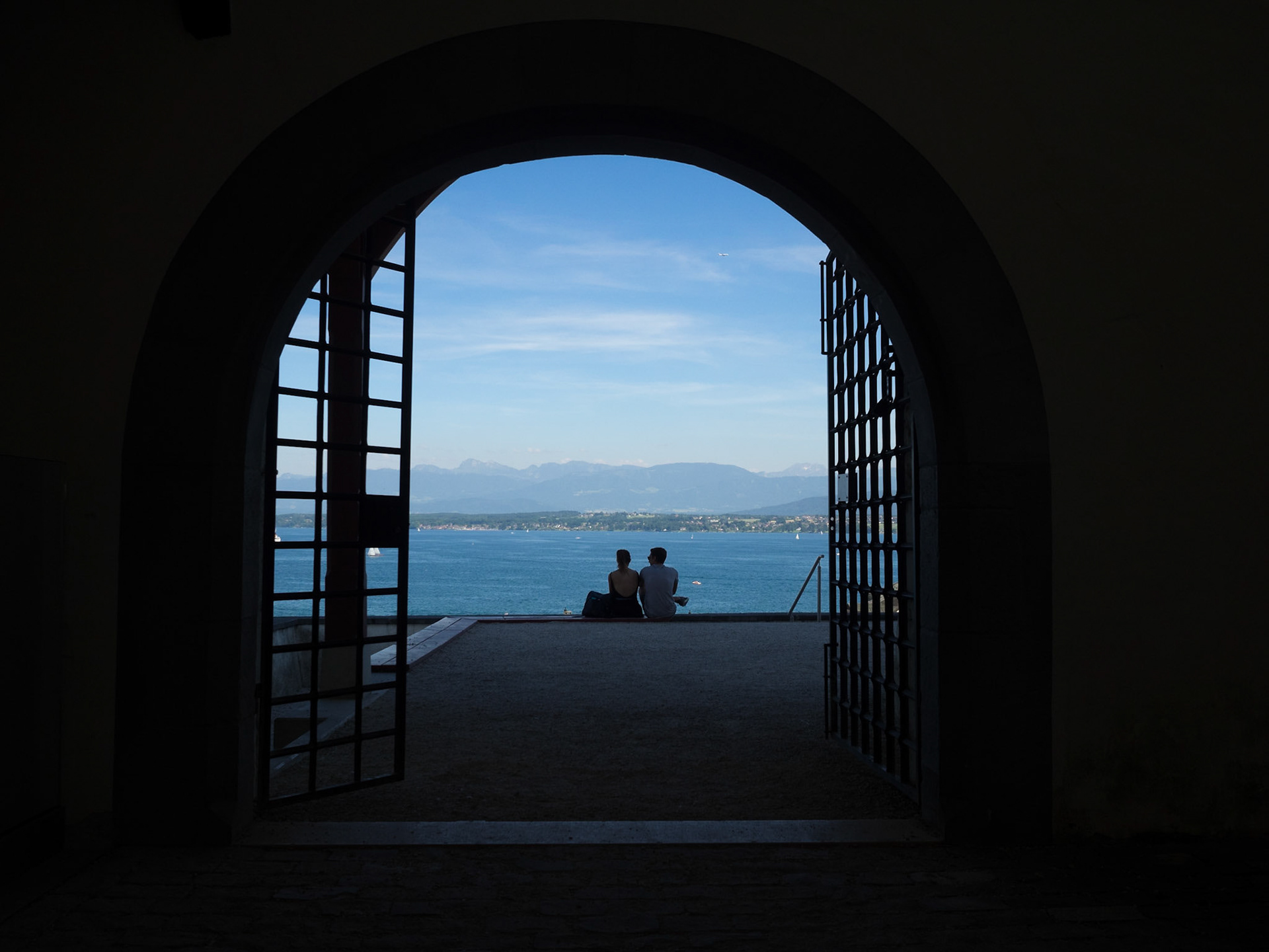 A couple silhouette facing Lake Geneva through a gate of Chateau de Nyon