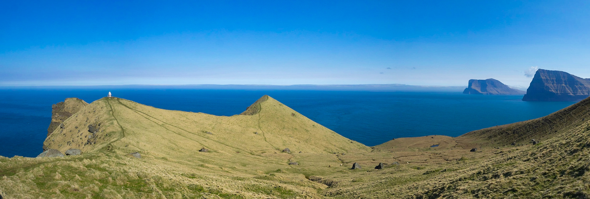 The hikking path by the cliffs edge leading to Kallur lighthouse, in north Kalsoy, with Kunoy and Vidoy islands in the horizon