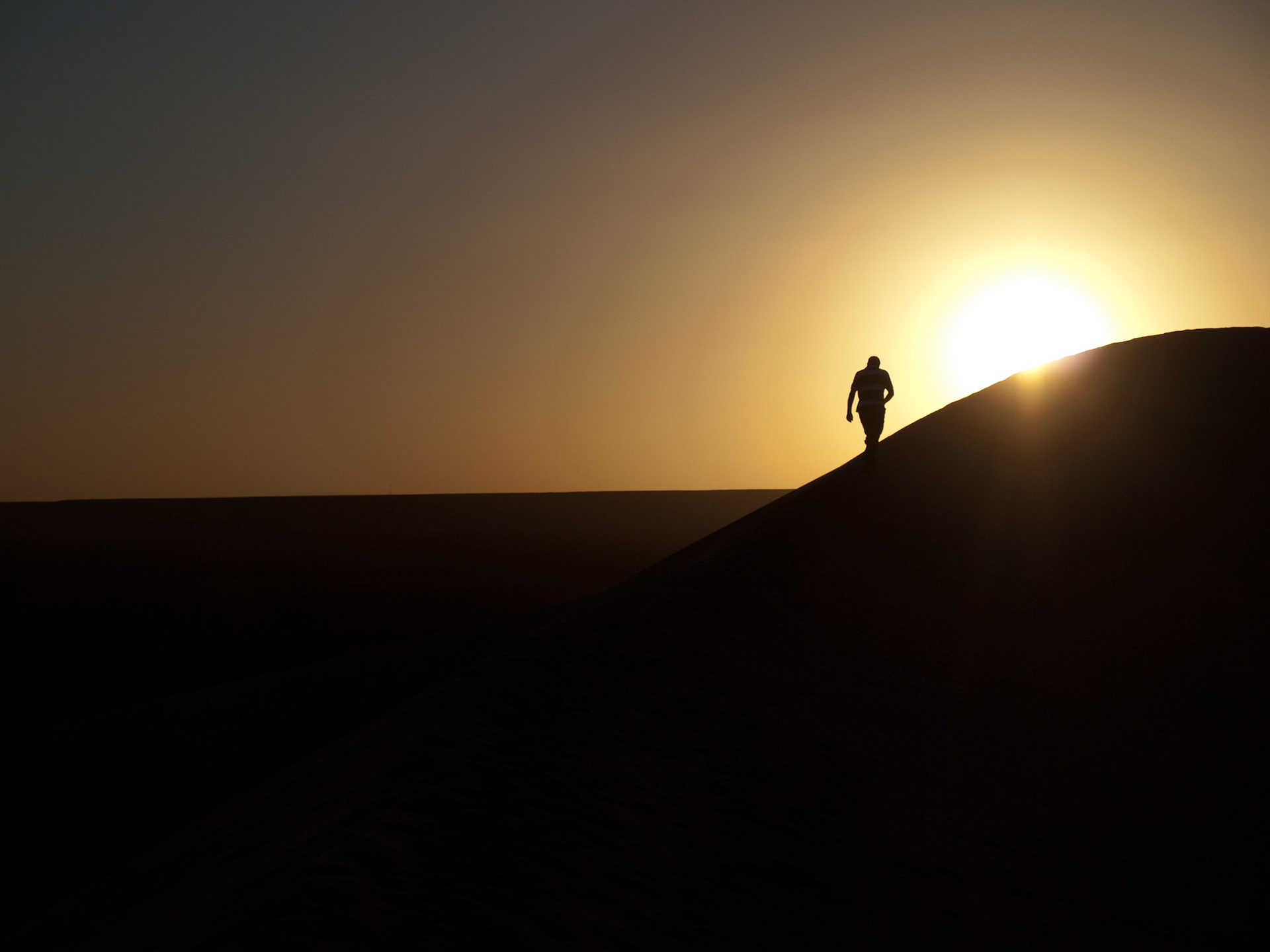 Man silhouette walking in sand dune at sunset