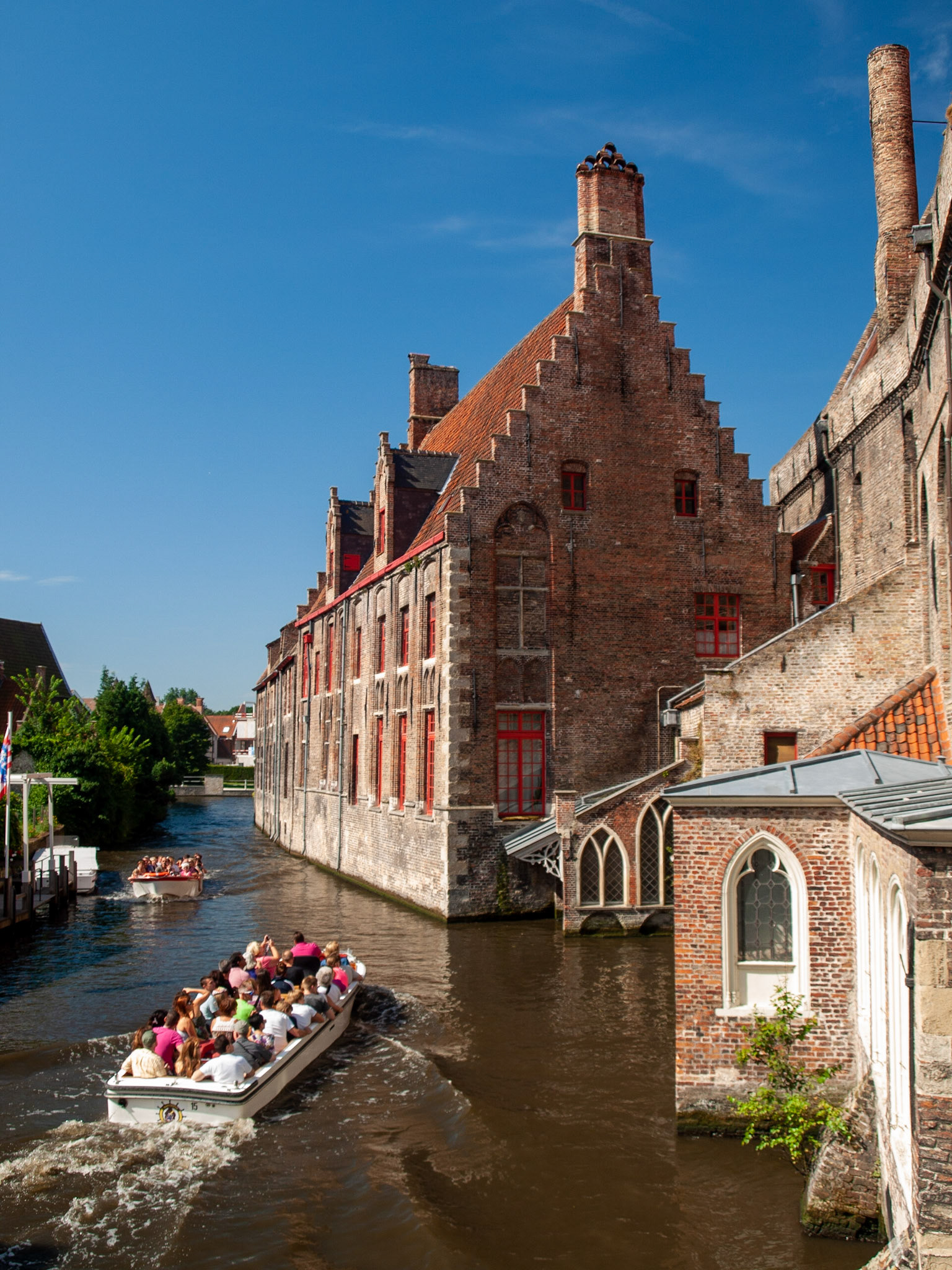Tourist boat in Bruges canal by St Janshospitaal building