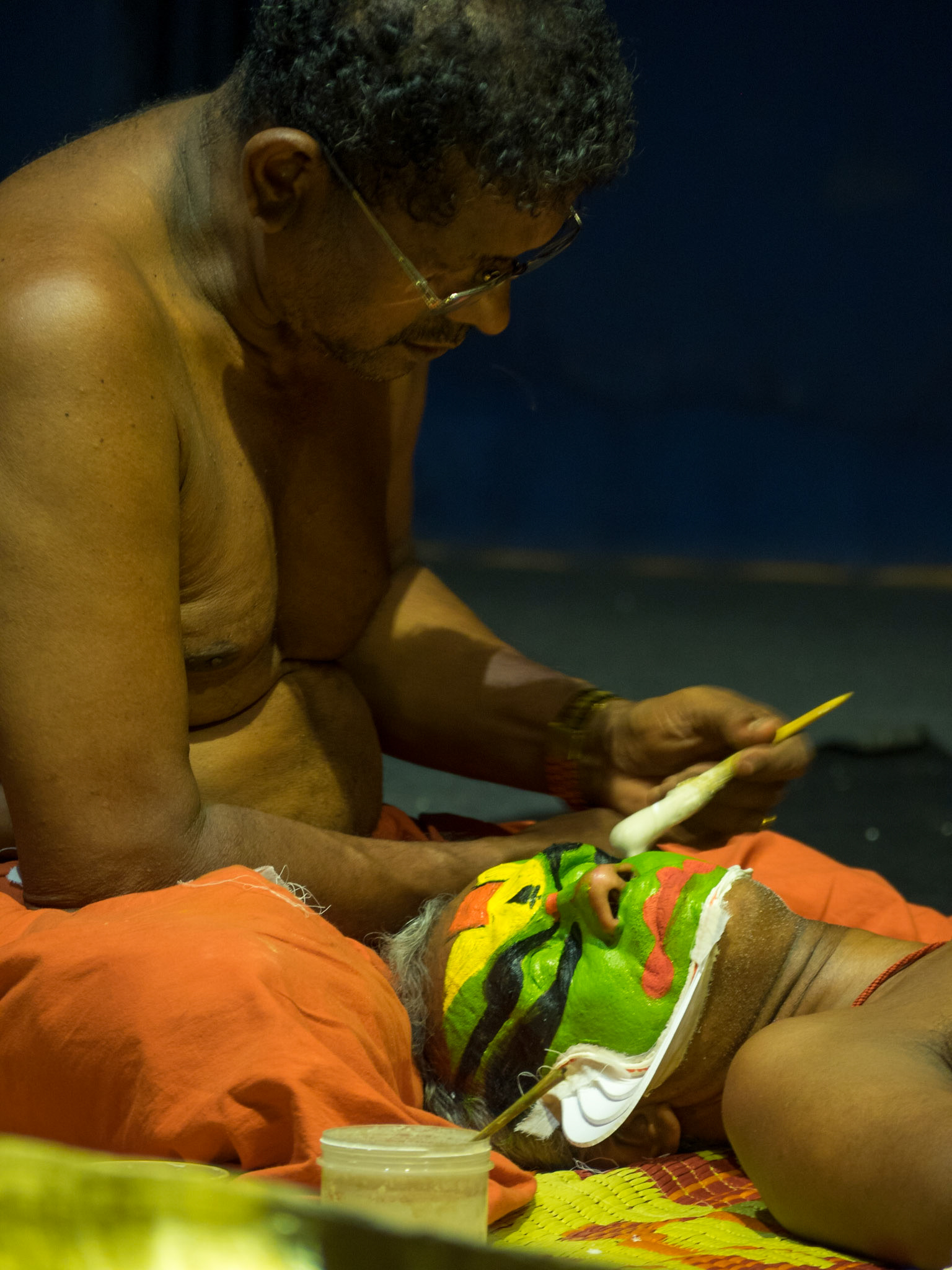 A man paints the face of a Kathakali performer just before the show