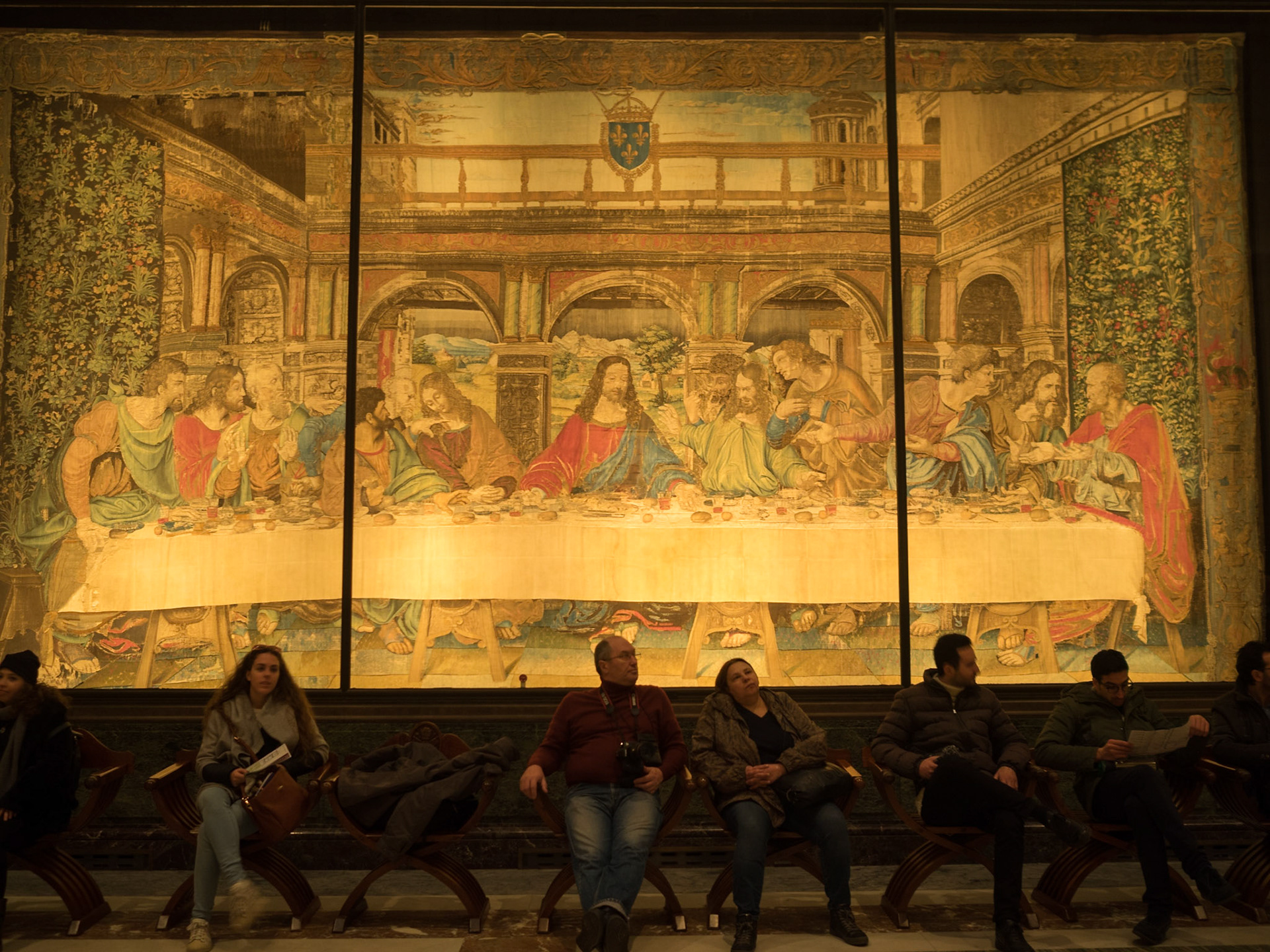 Vatican Museum visitors seated resting in front of a Last Supper tapestry