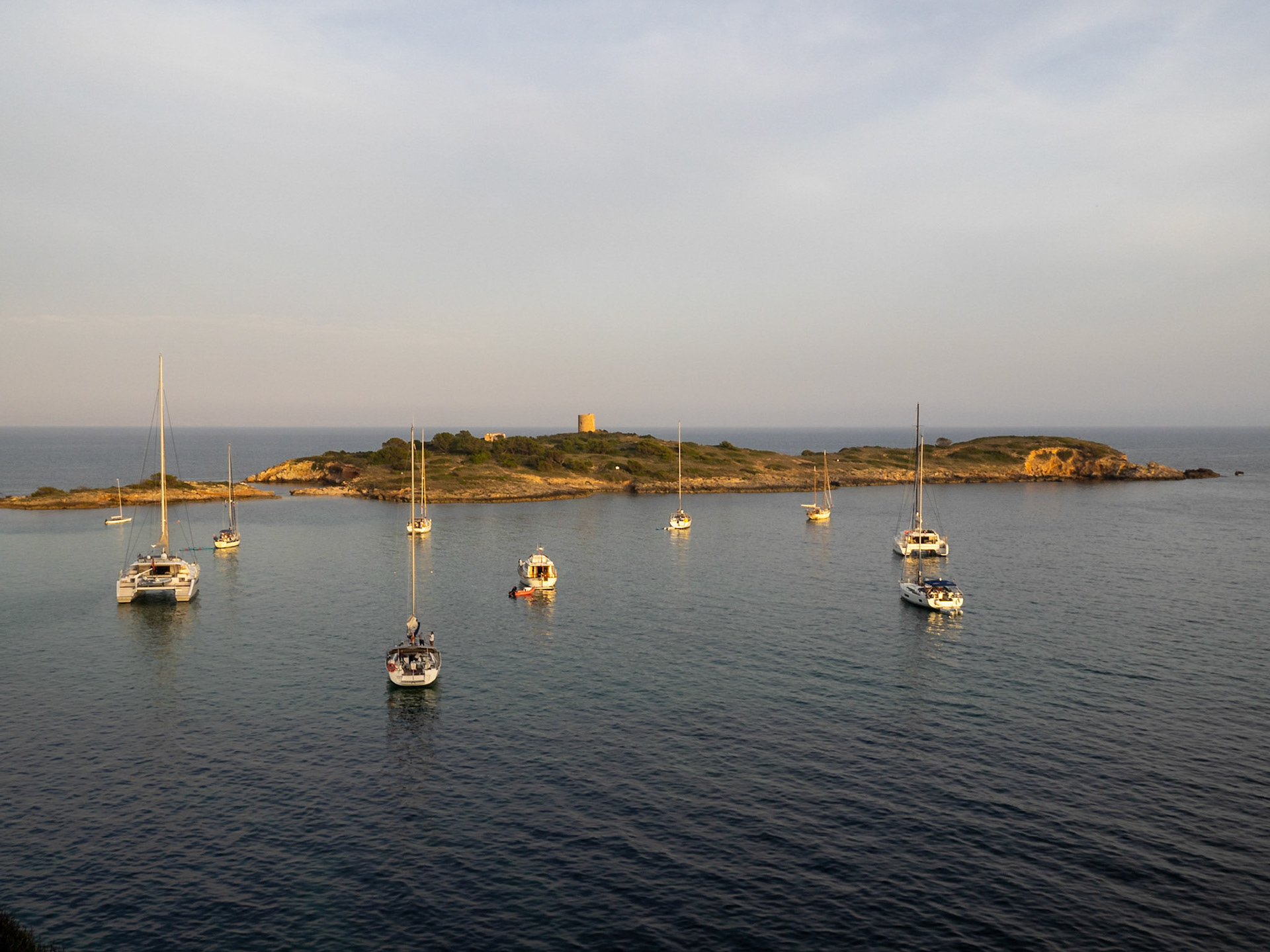 Sailboats floating by Isla de Sa Torre at dusk, Maiorca