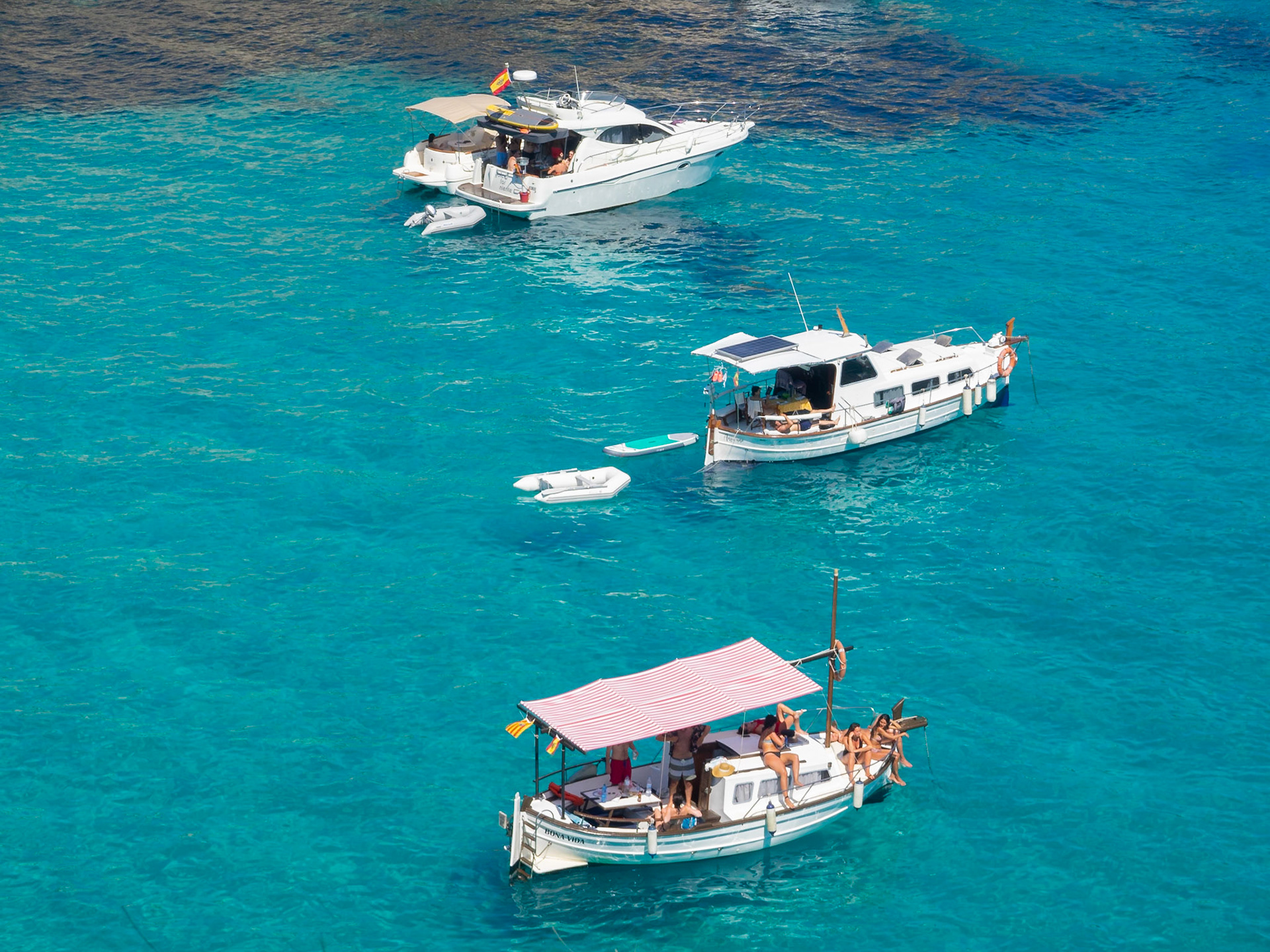Sunbathing on the boats floating over the turquoise waters of Cala Macarelleta, Menorca