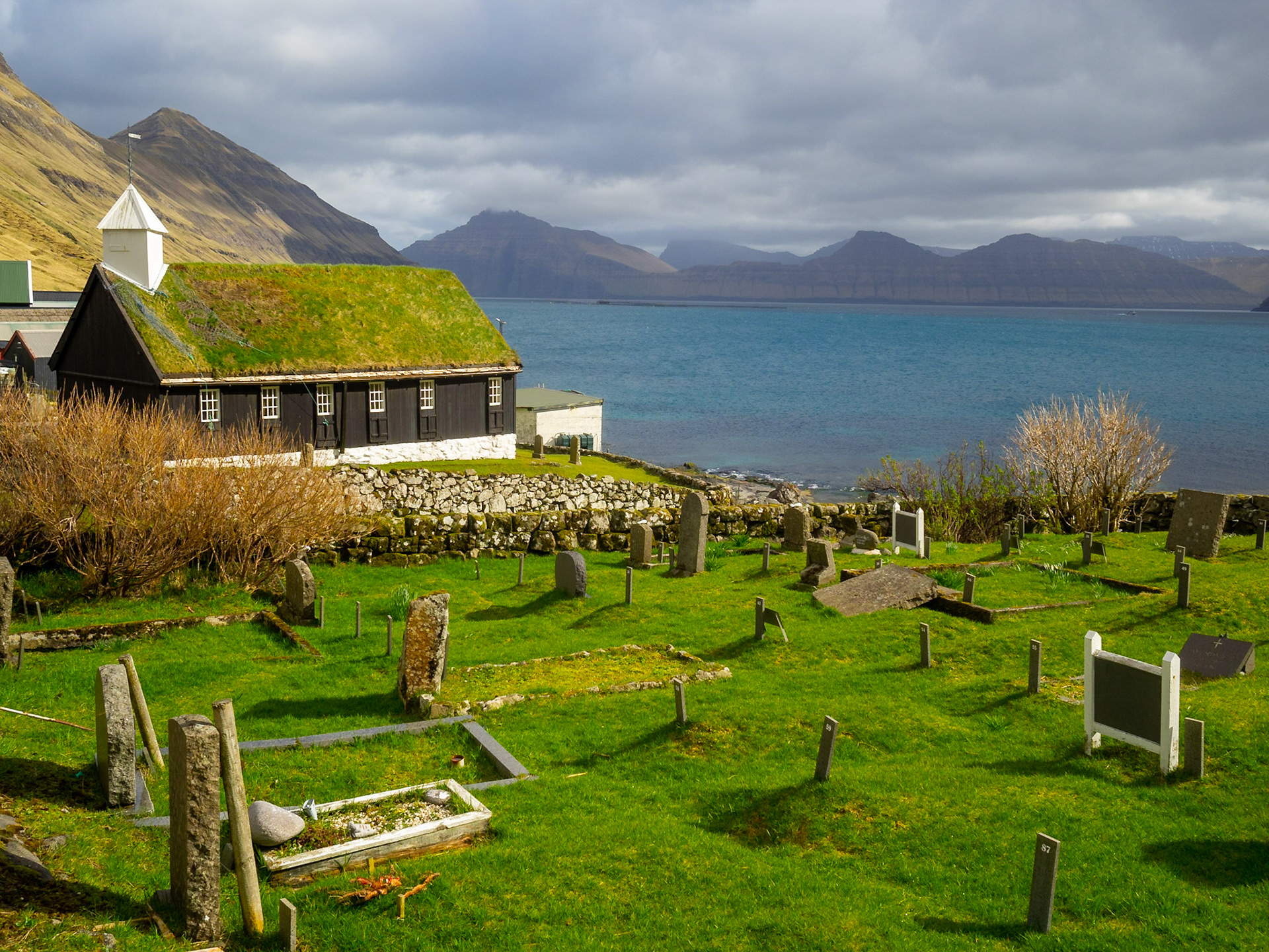 Funningur black turf rooffed wooden church and graveyard by the fjord