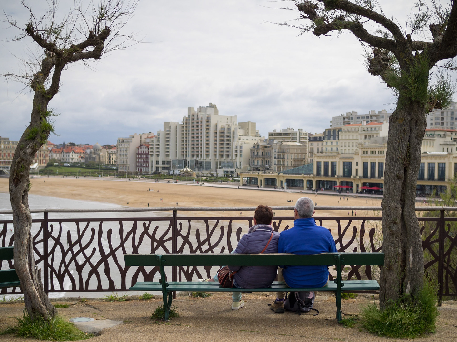 A couple seating in a bench looking at Biarritz beach