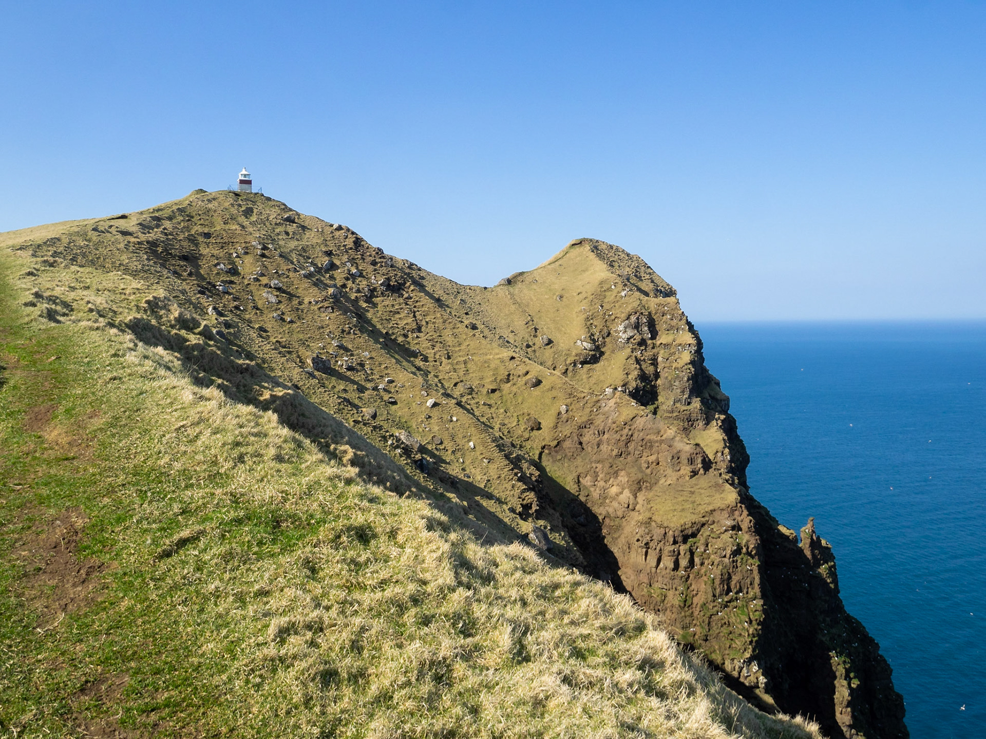 Kallur lighthouse at the end of the hiking path, by the cliffs edge of north Kalsoy