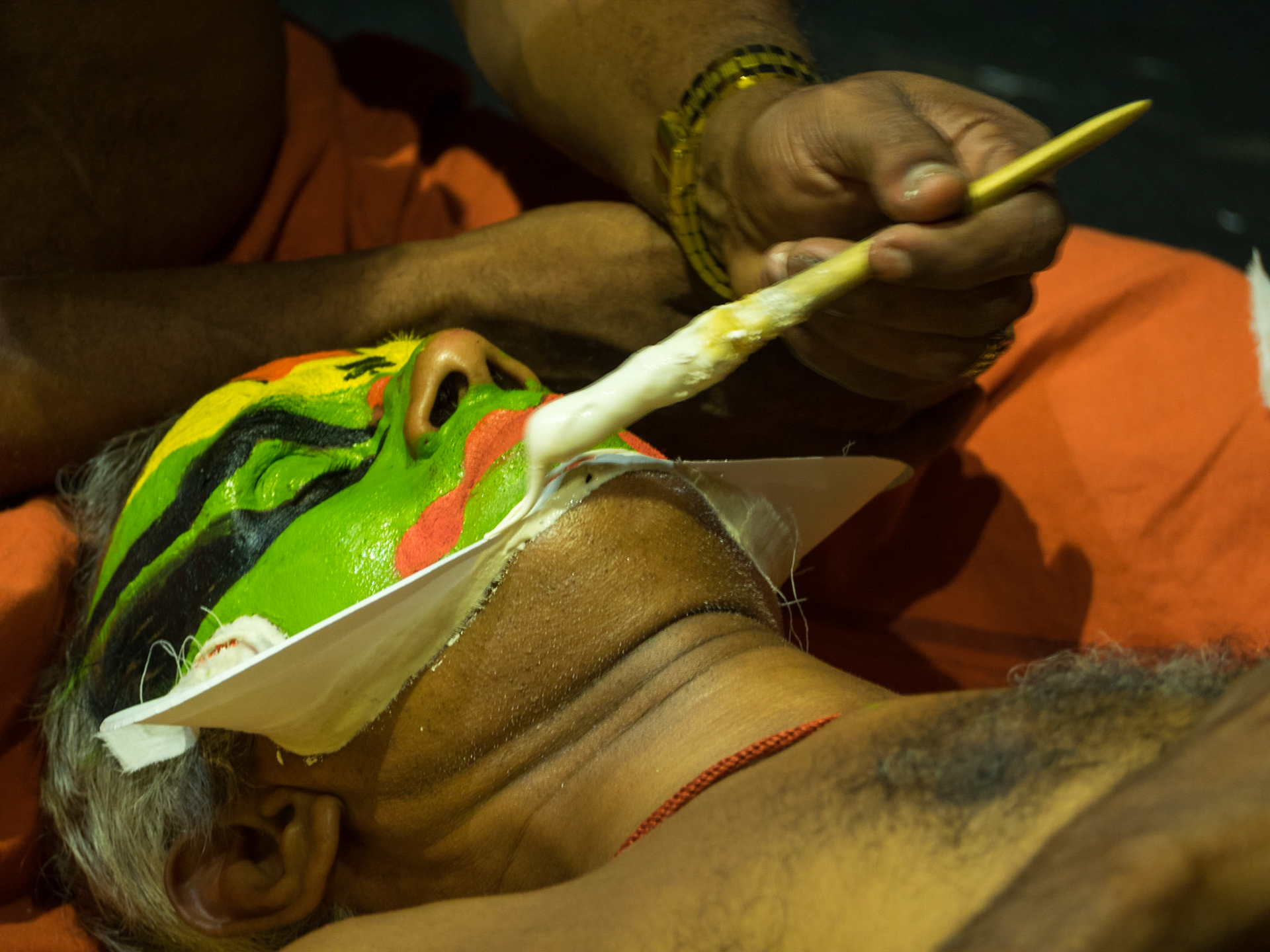 A man paints the face of a Kathakali performer just before the show