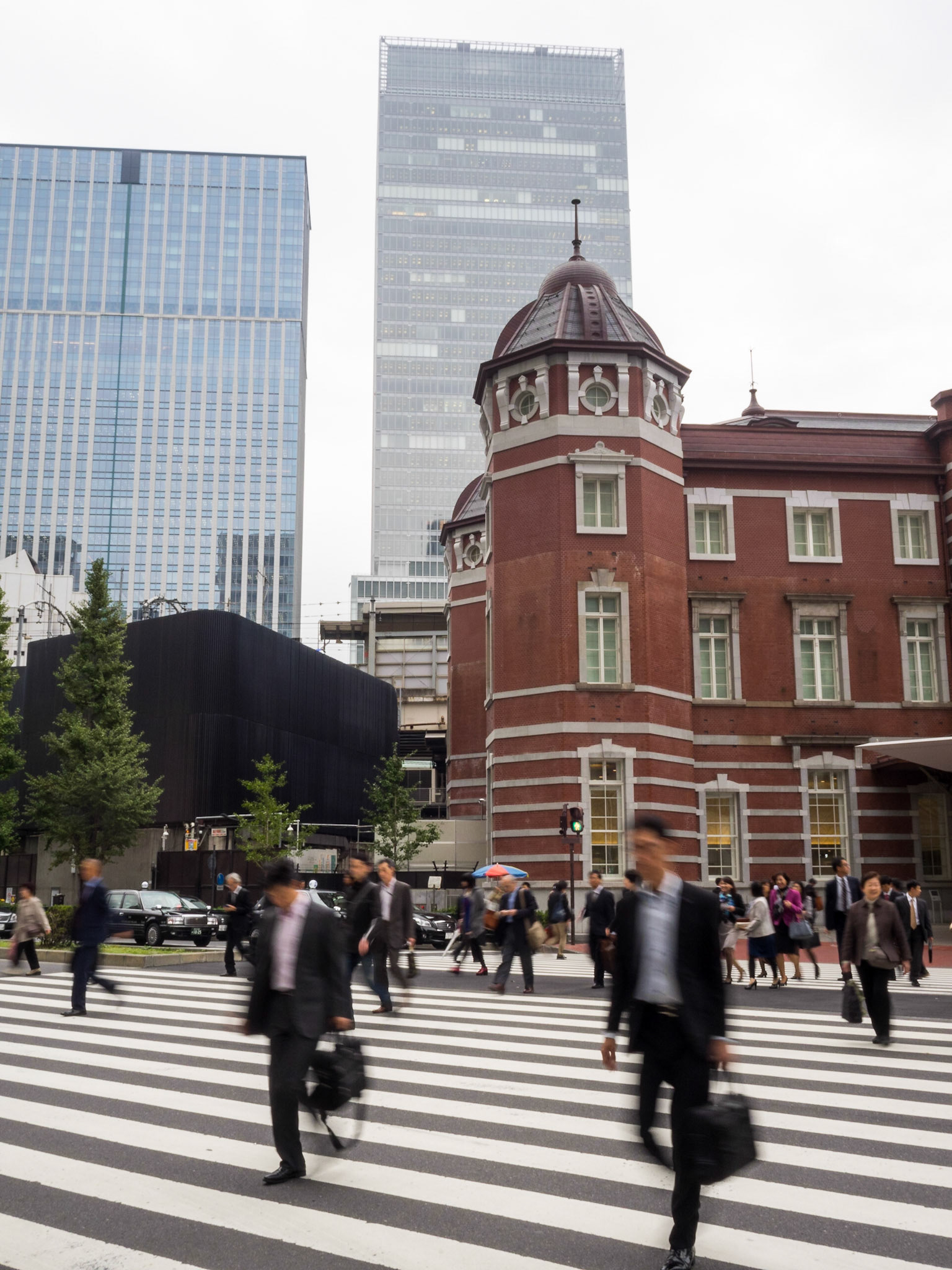 Salary man in suite and white shirt crossing the street at Tokyo Station with skyscrapers in background