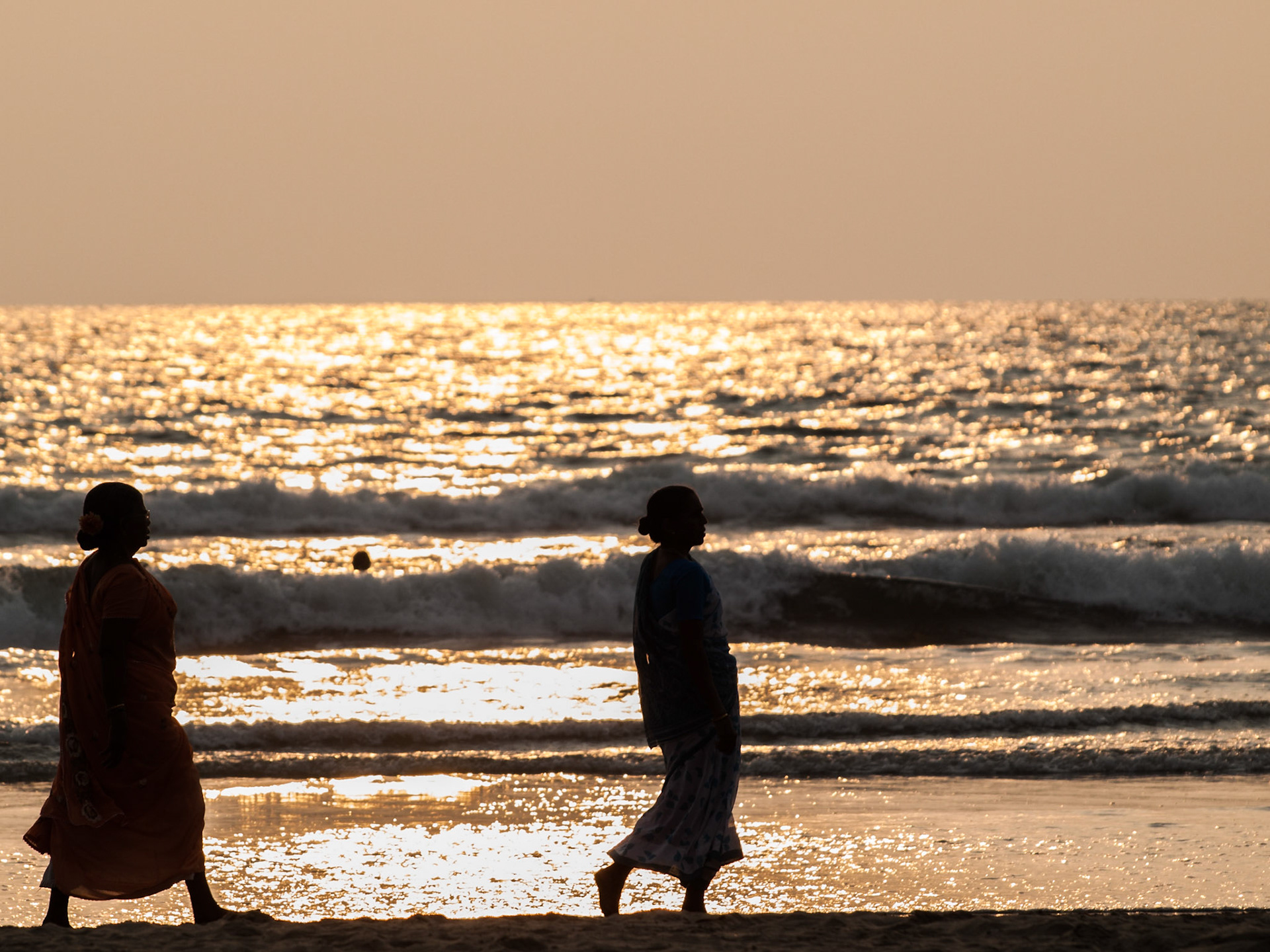 Indian women silhouettes by the sea in the sunset light at Mandrem beach