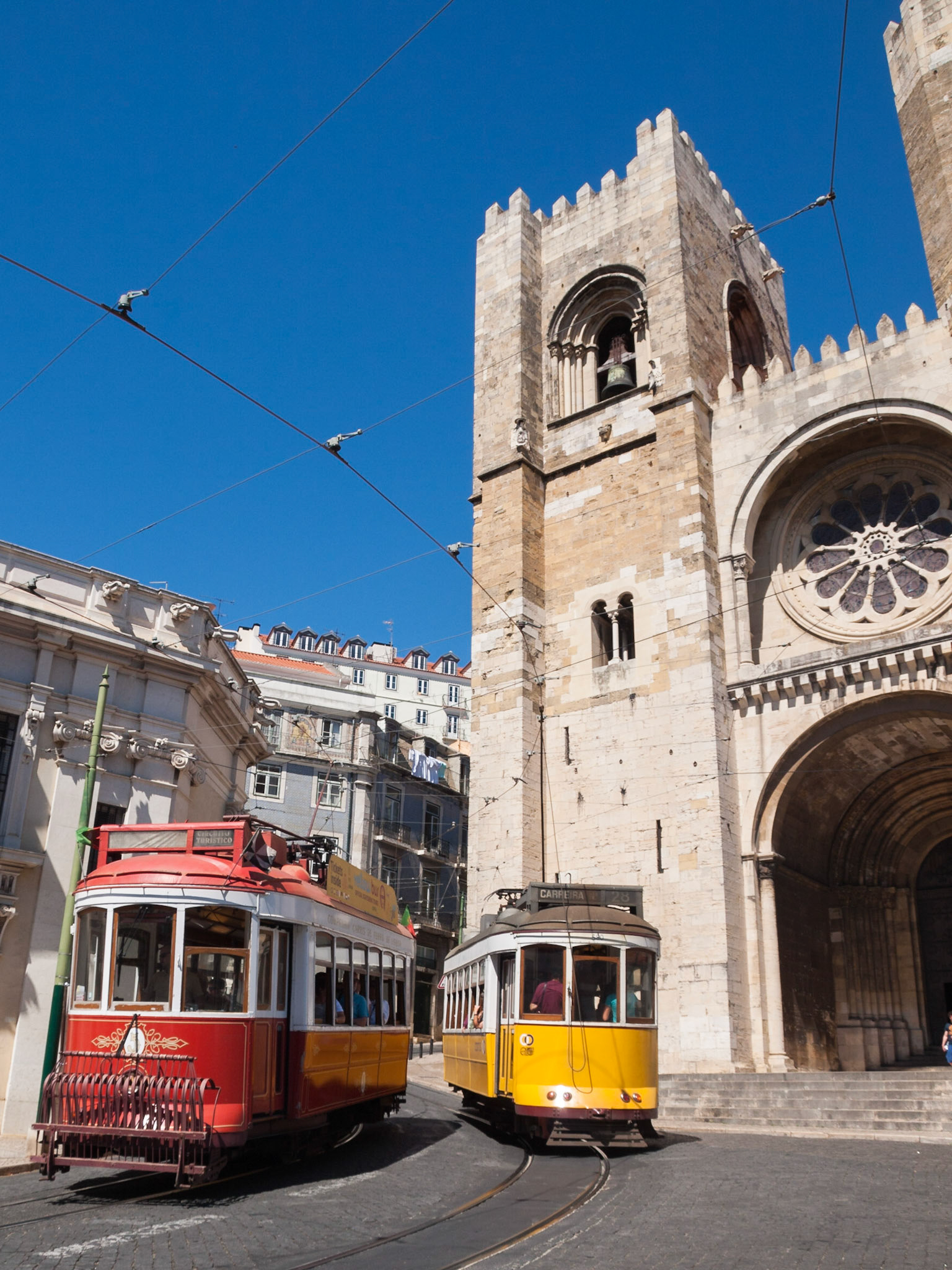 Trams pass by Lisbon Sé cathedral facade
