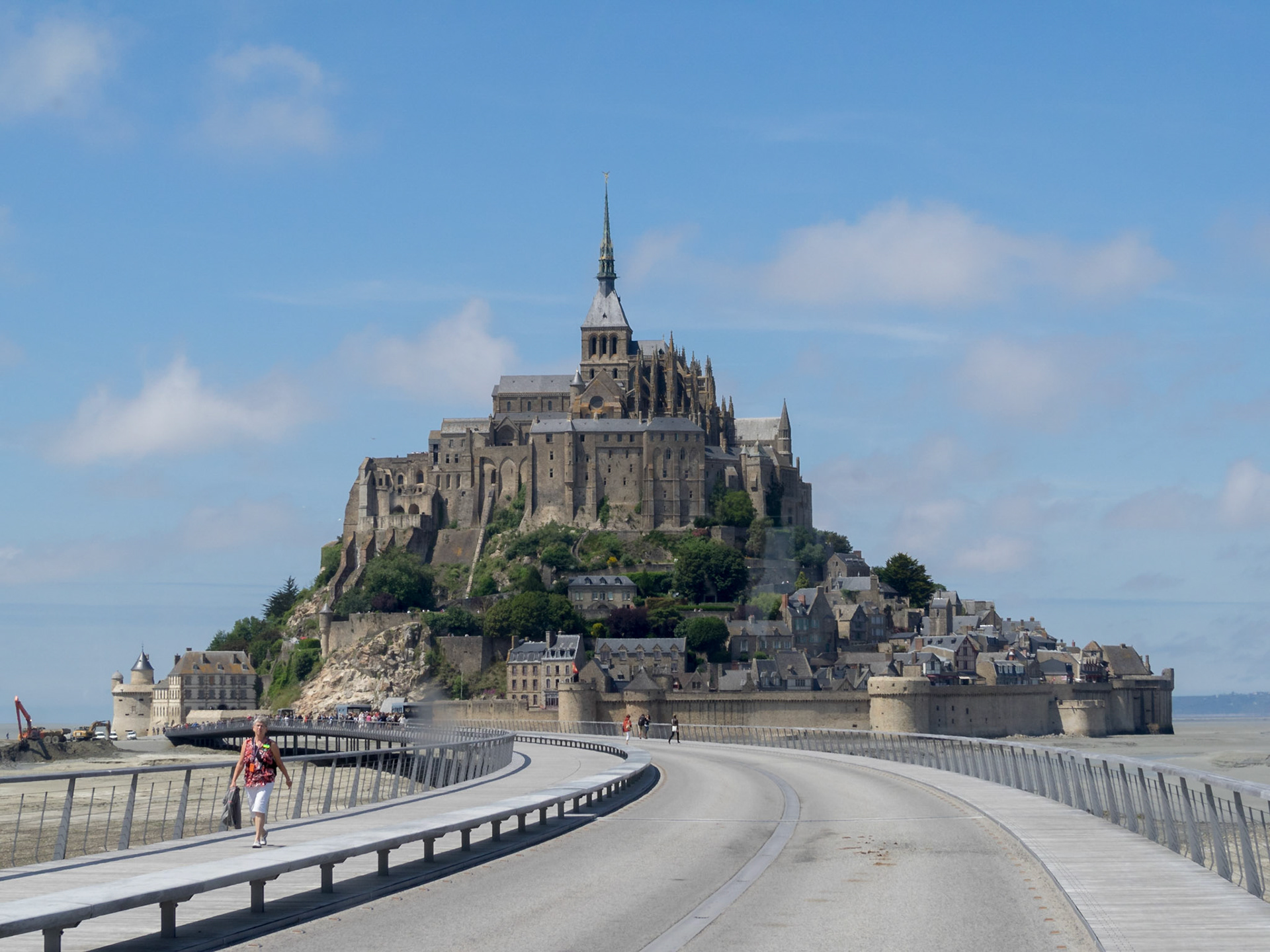 A tourist walks on the bridge from Mont Saint-Michel