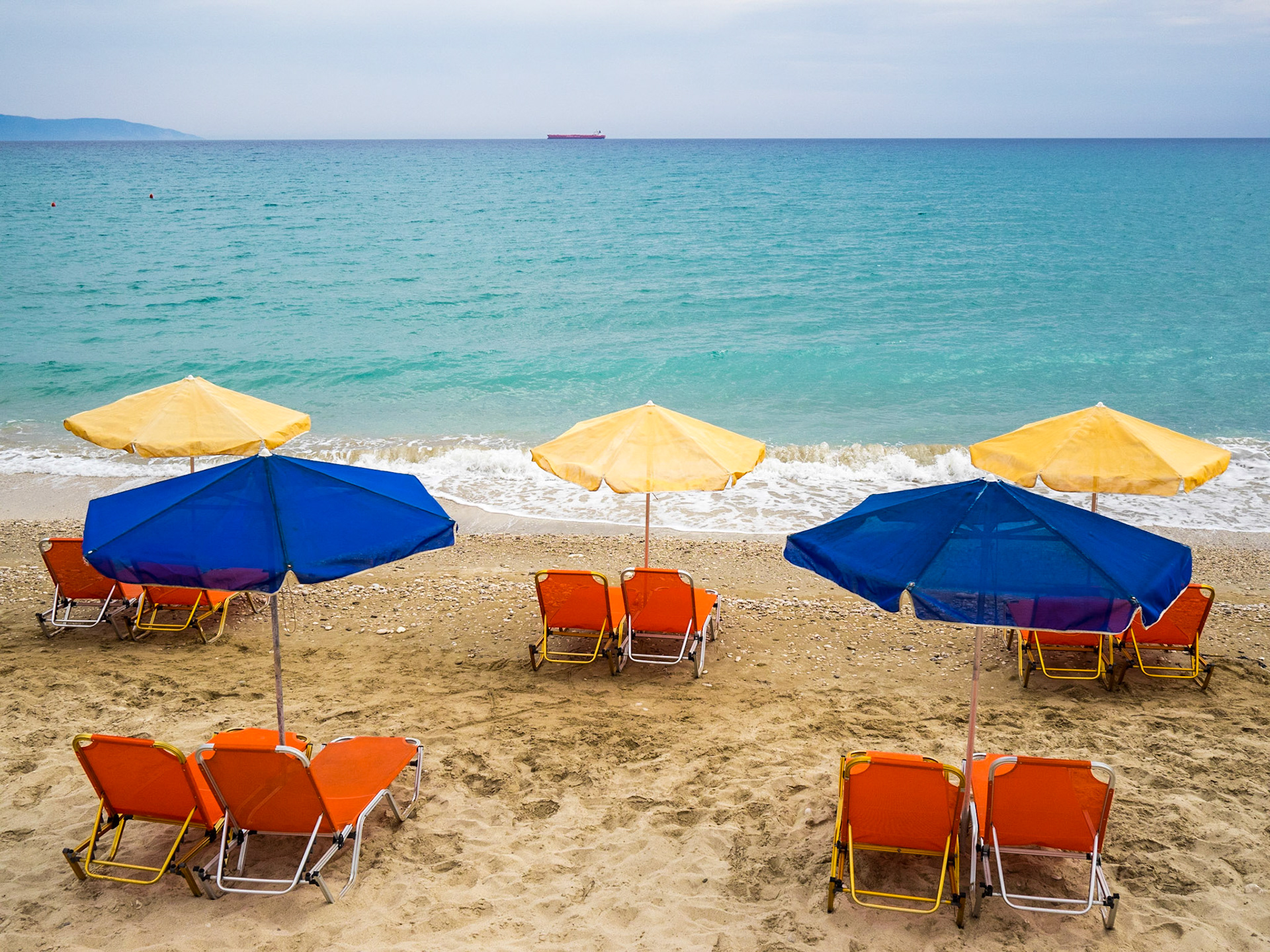 Colorful sun umbrellas and beds by the turquoise sea of Lourdata beach in Kefalonia island