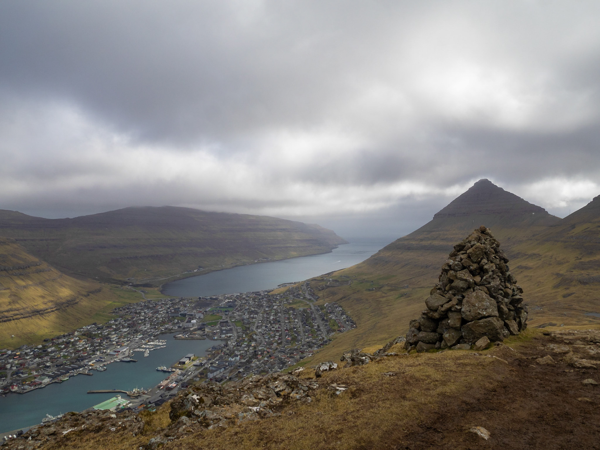 A cairn on top of Klakkur mountain hiking path, with Klaksvik below in the horizon