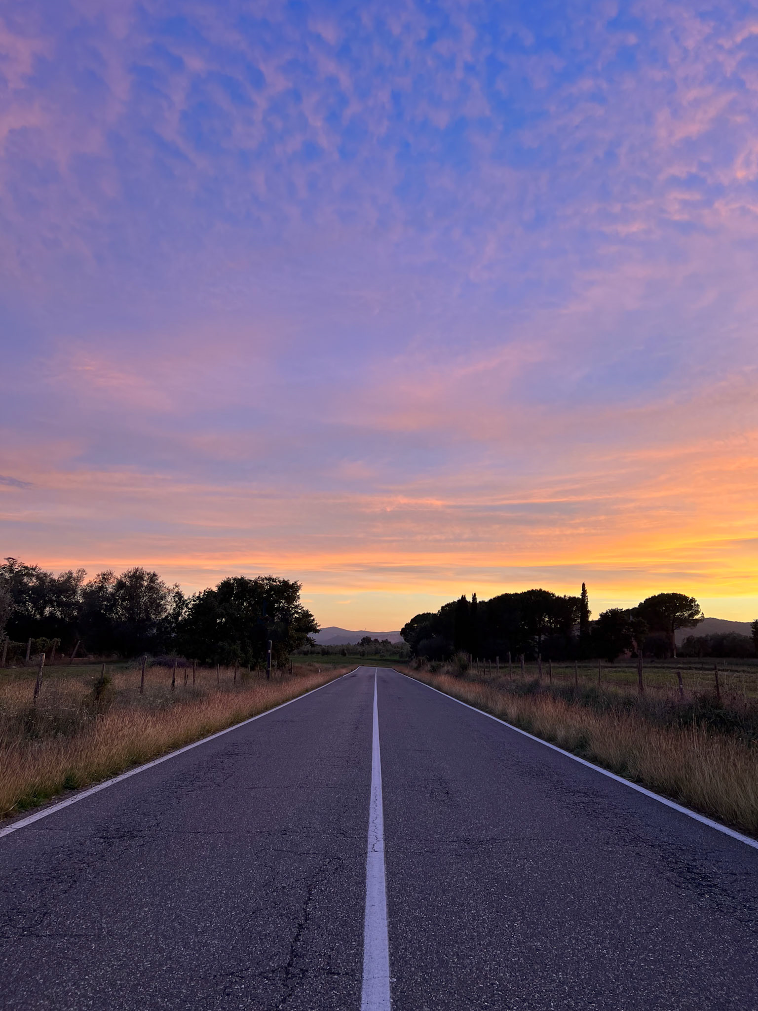 Purple and orange sunset sky in Tuscany, above a countryside road