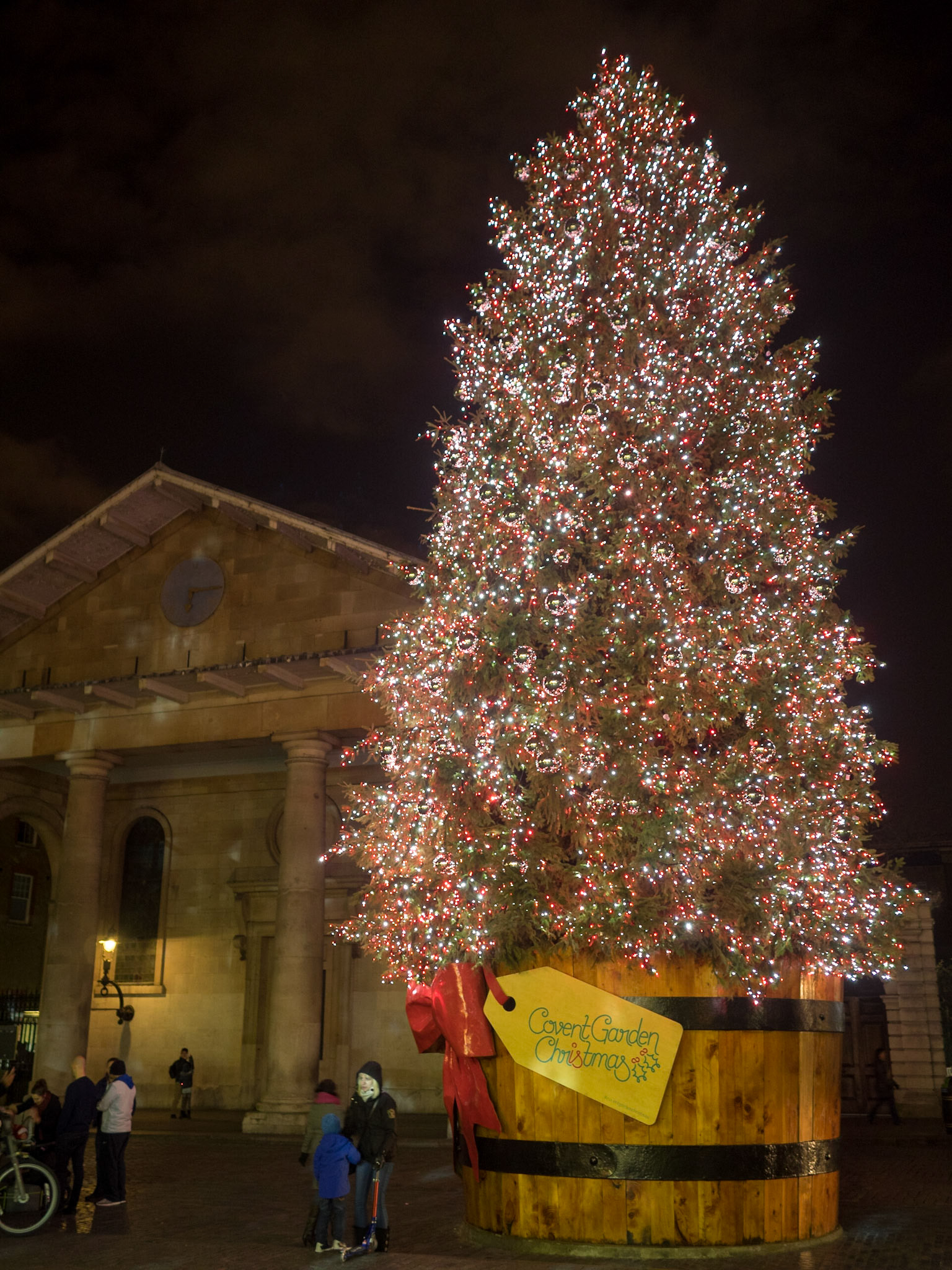 People taking pictures at night by the glowing Christmas tree of Covent Garden
