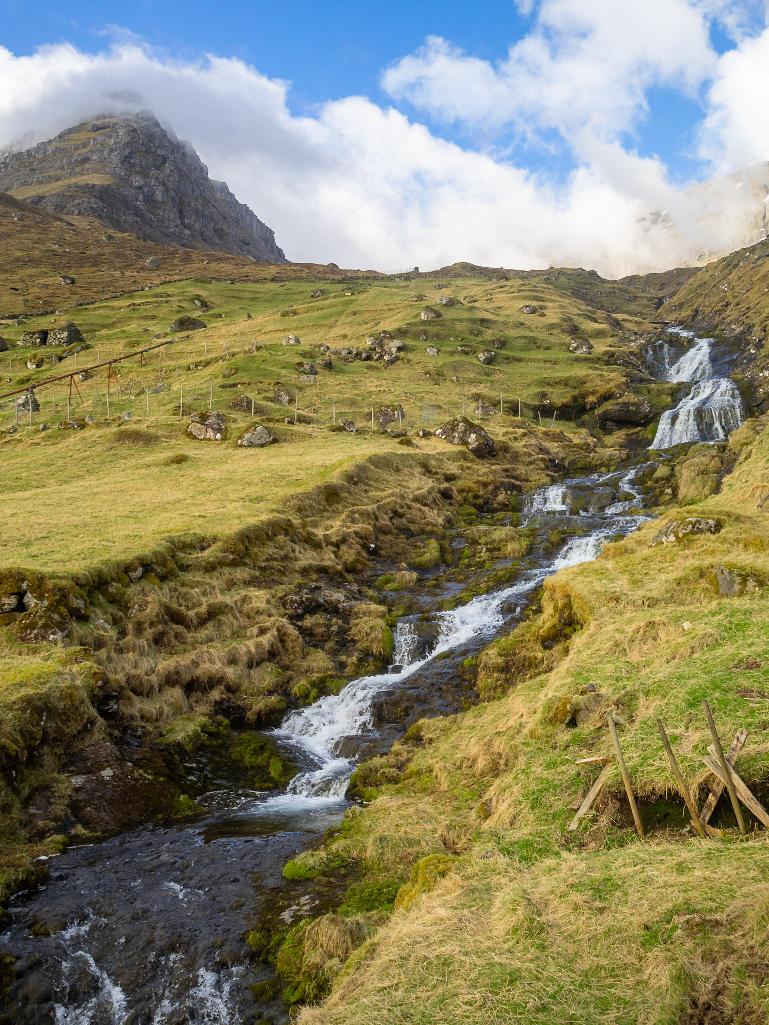 Waterfall tumbling down the mountain between the grass fileds of Kunoy island