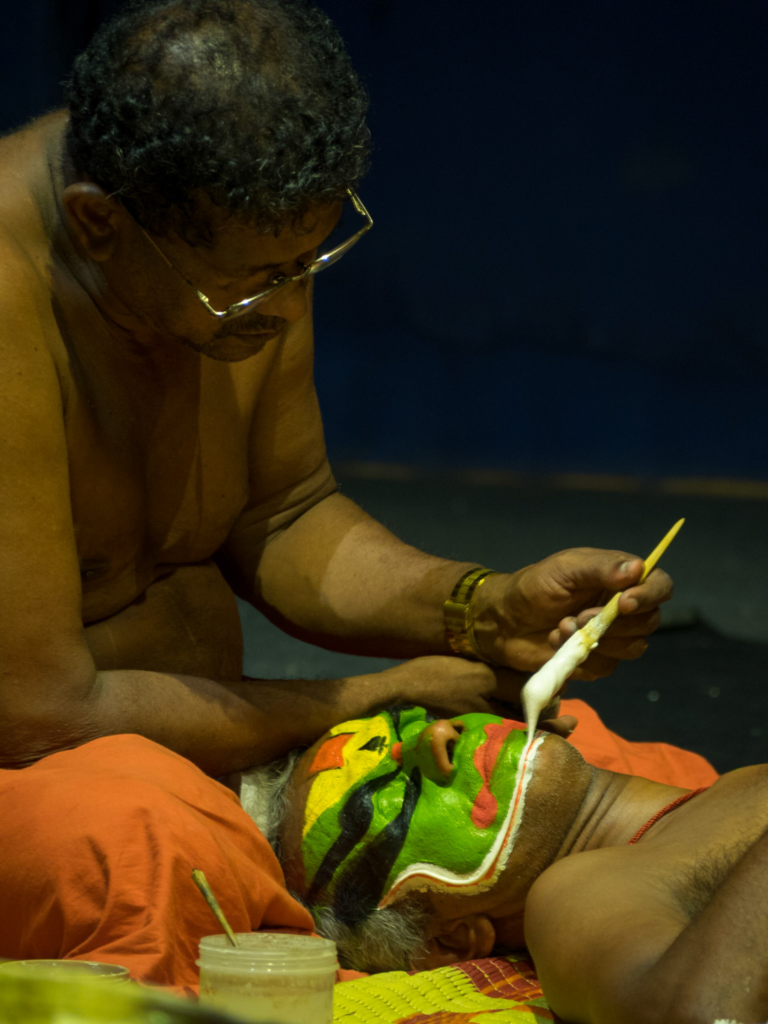 A man paints the face of a Kathakali performer just before the show
