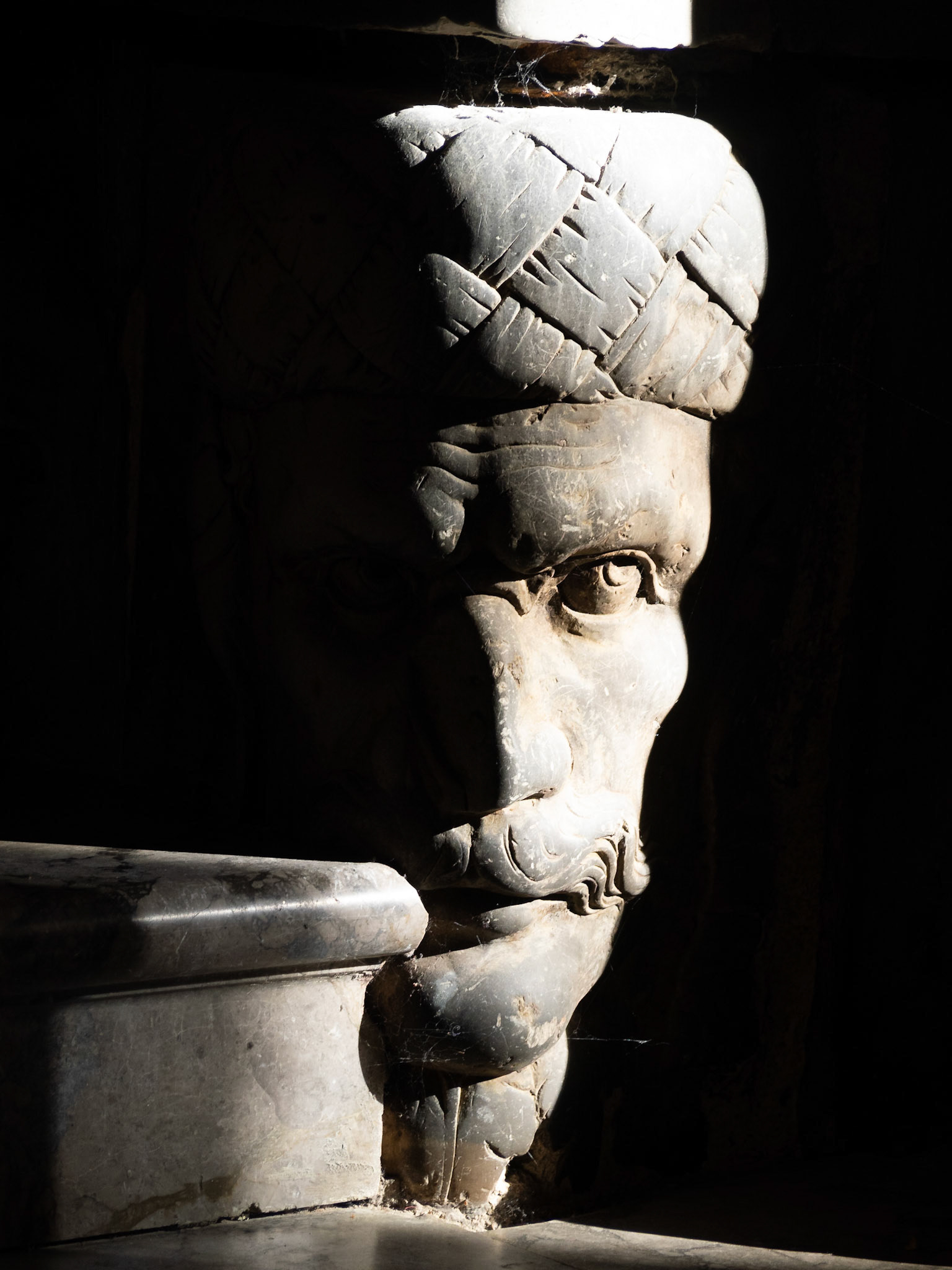 Detail of a man head with turban carved in stone in the base of a column in Enna Cathedral