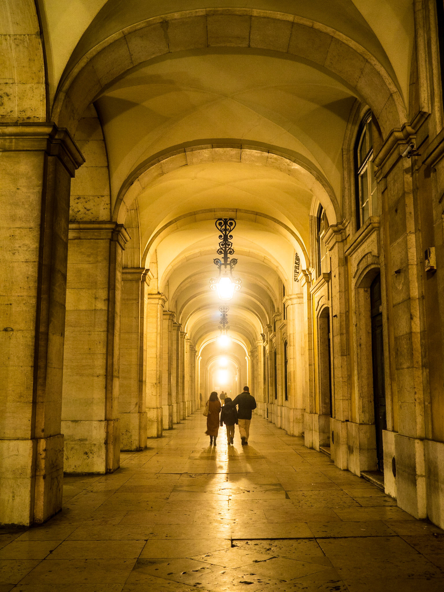 People walk under the Lisbon downtown archays in a foggy night