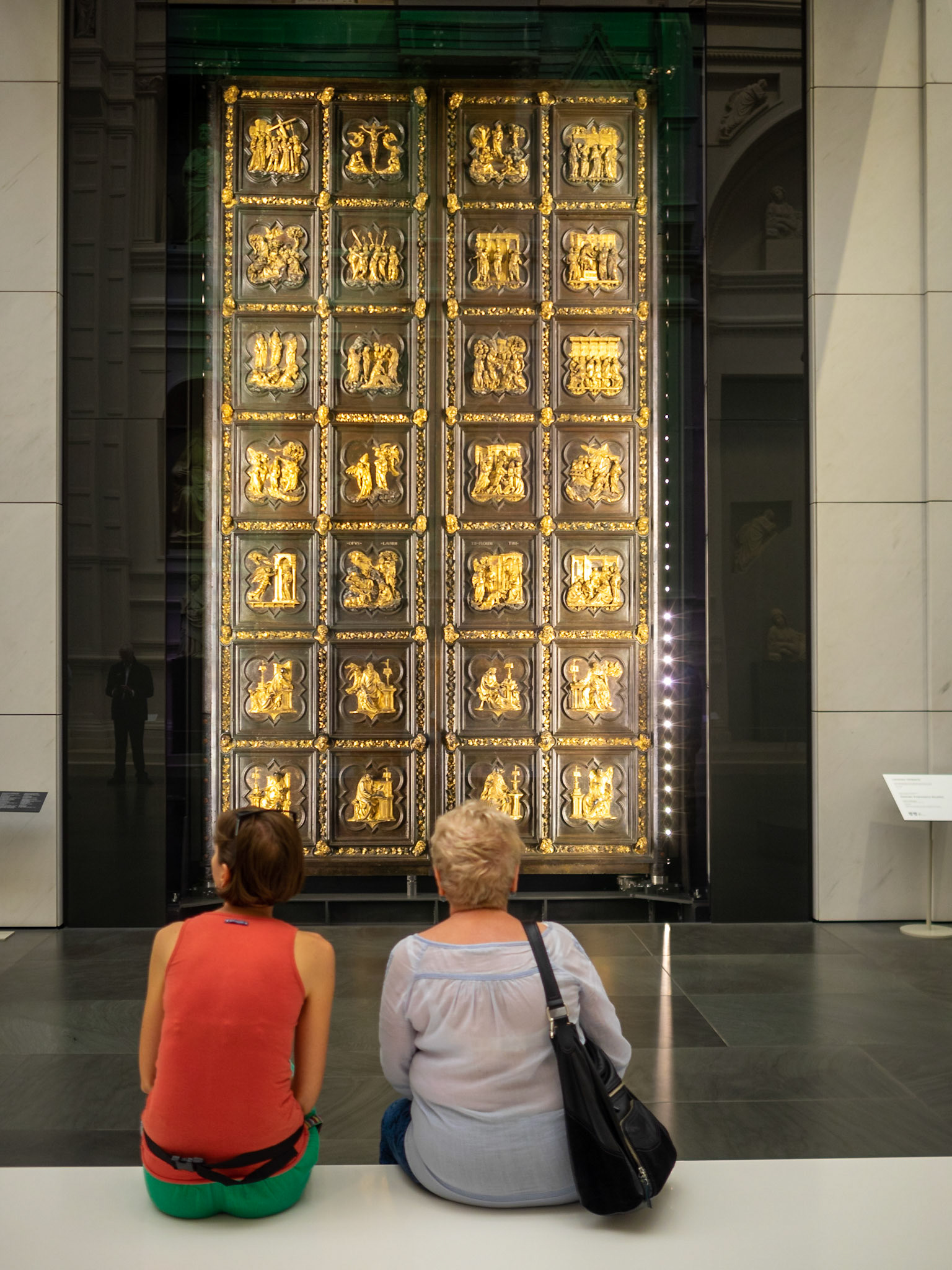 Two tourists admire the original North doors, by Lorenzo Ghiberti, from the Florence Duomo, in the museum of the cathedral