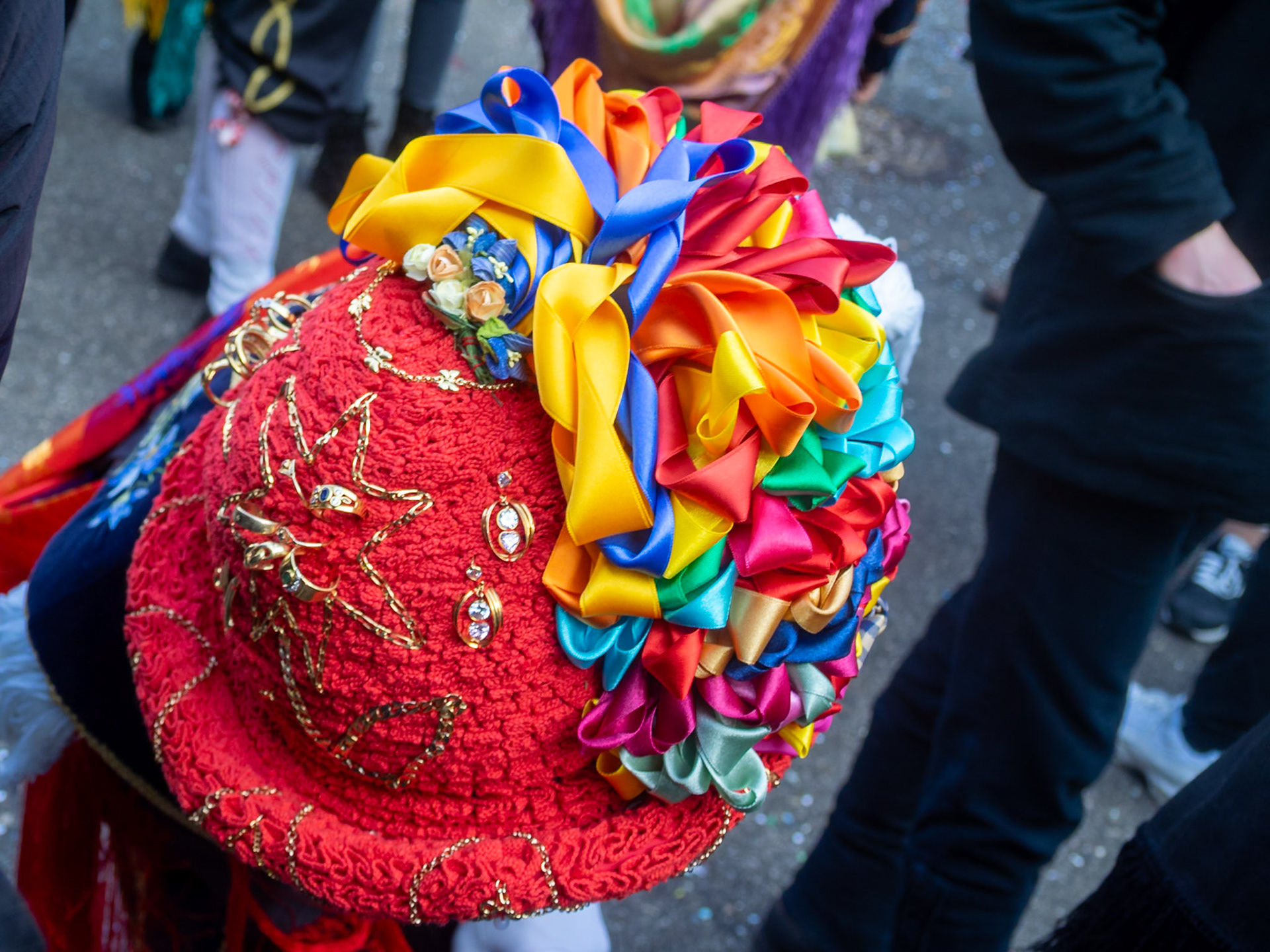 Top view of a Balarì felt hat, covered in a red folded ribbon,  decorated with embroidery, gold jewels, from the family or borrowed, and multicoloured ribbons in a bow shape, Bagolino Carnival