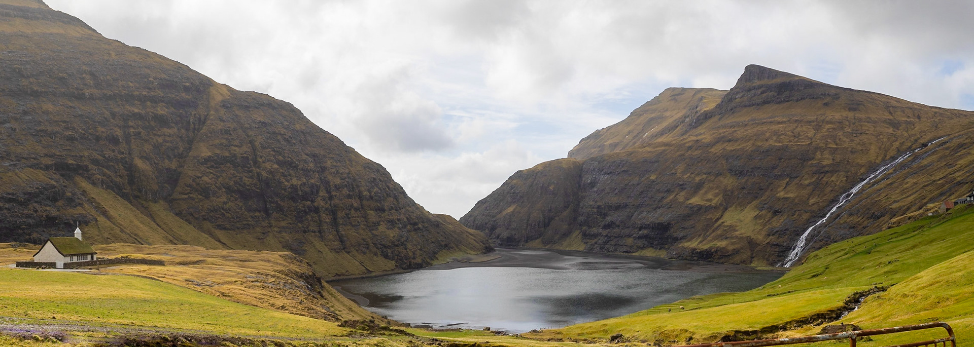 Panorama of Saksun tidal lagoon with green fields and the turf roofed church