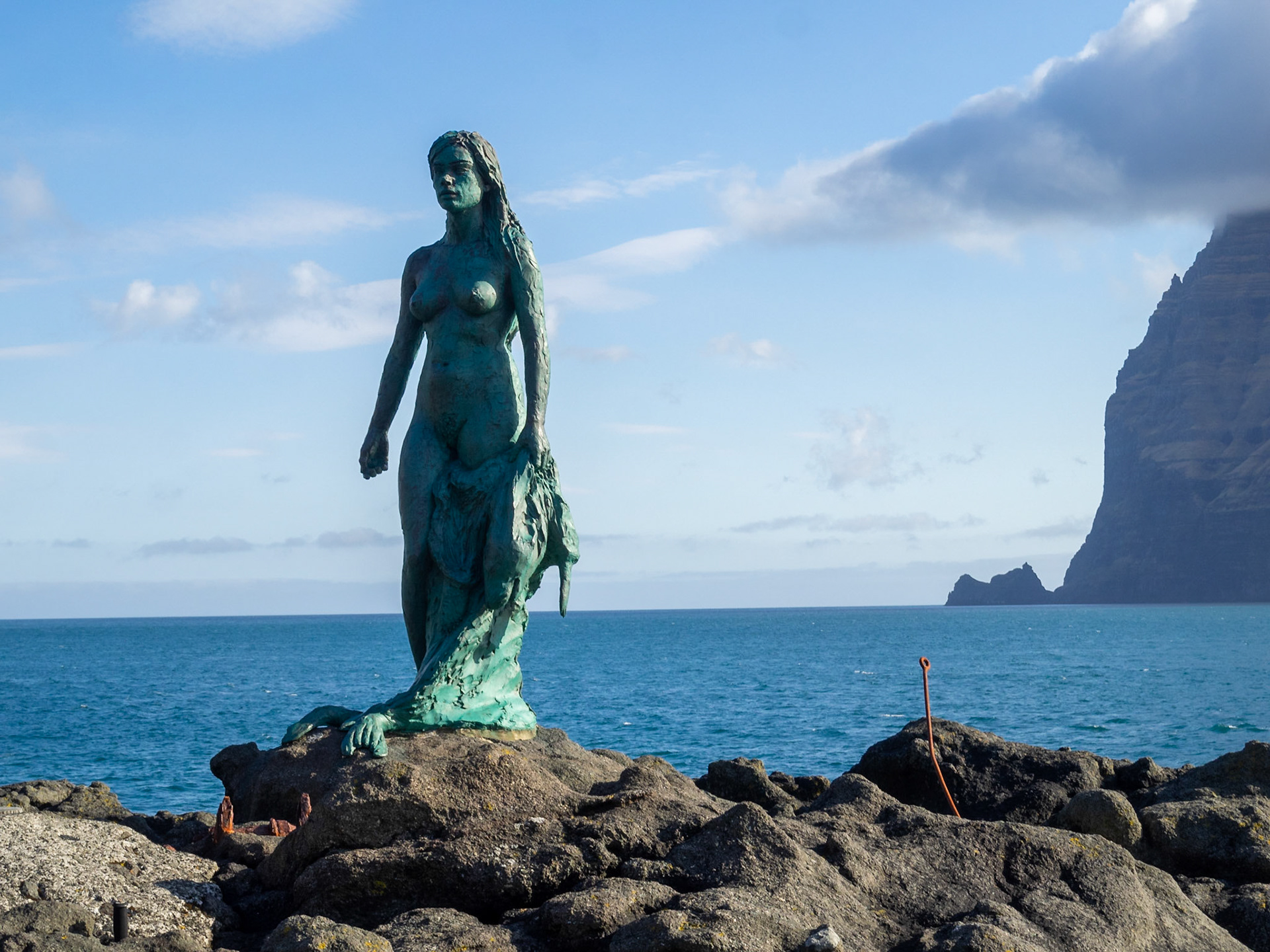 Kópakonan, the seal woman, statue over the rocks by the Kalsoyarfjørður fjord with Kynoy island in background