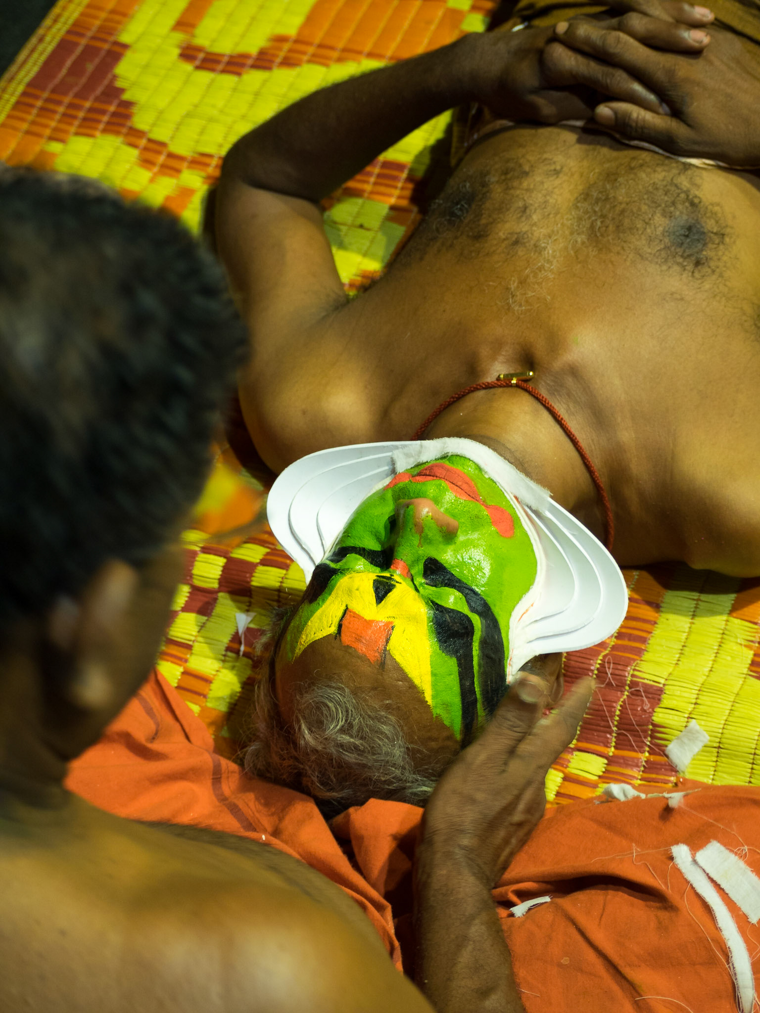 A man paints the face of a Kathakali performer just before the show