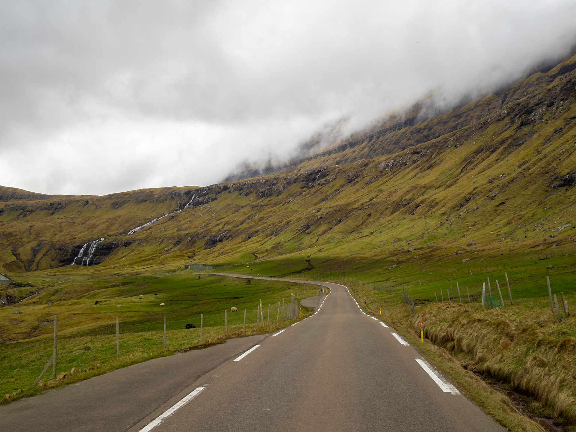 Oyndarfjørður fjord road with a waterfall tumbling down the mountain