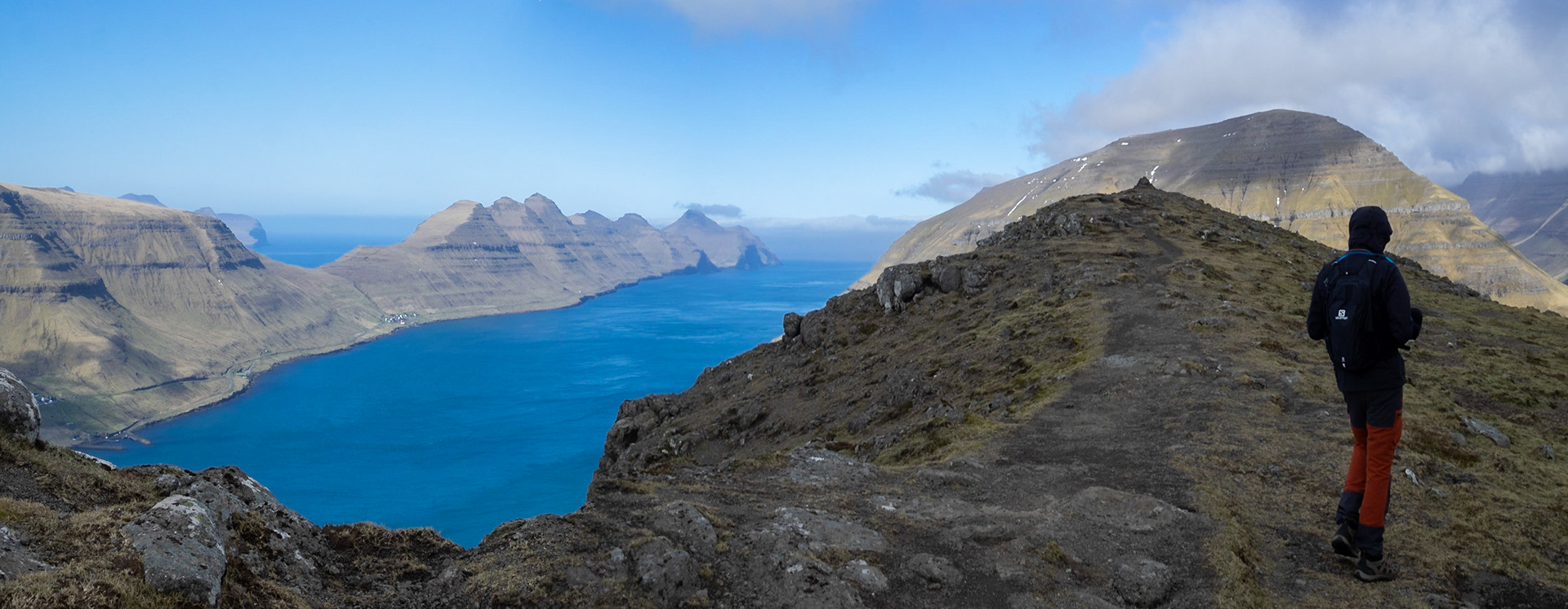 A man trekking in Klakkur mountain with Kalsoy and Kalsoyarfjørður on the horizon