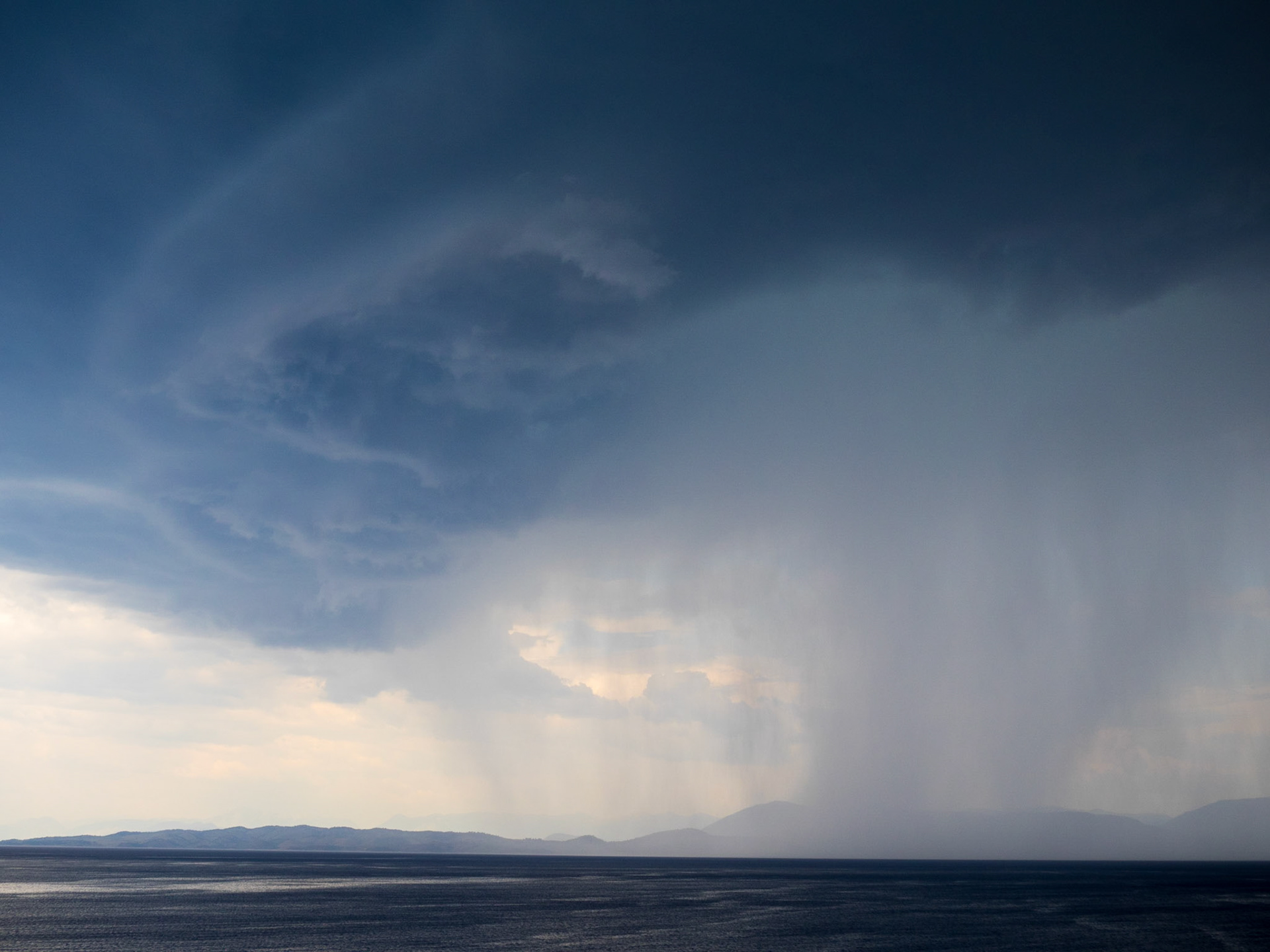 Heavy rain and dark stormy clouds over the Ionian sea between continental Greece and Corfu island