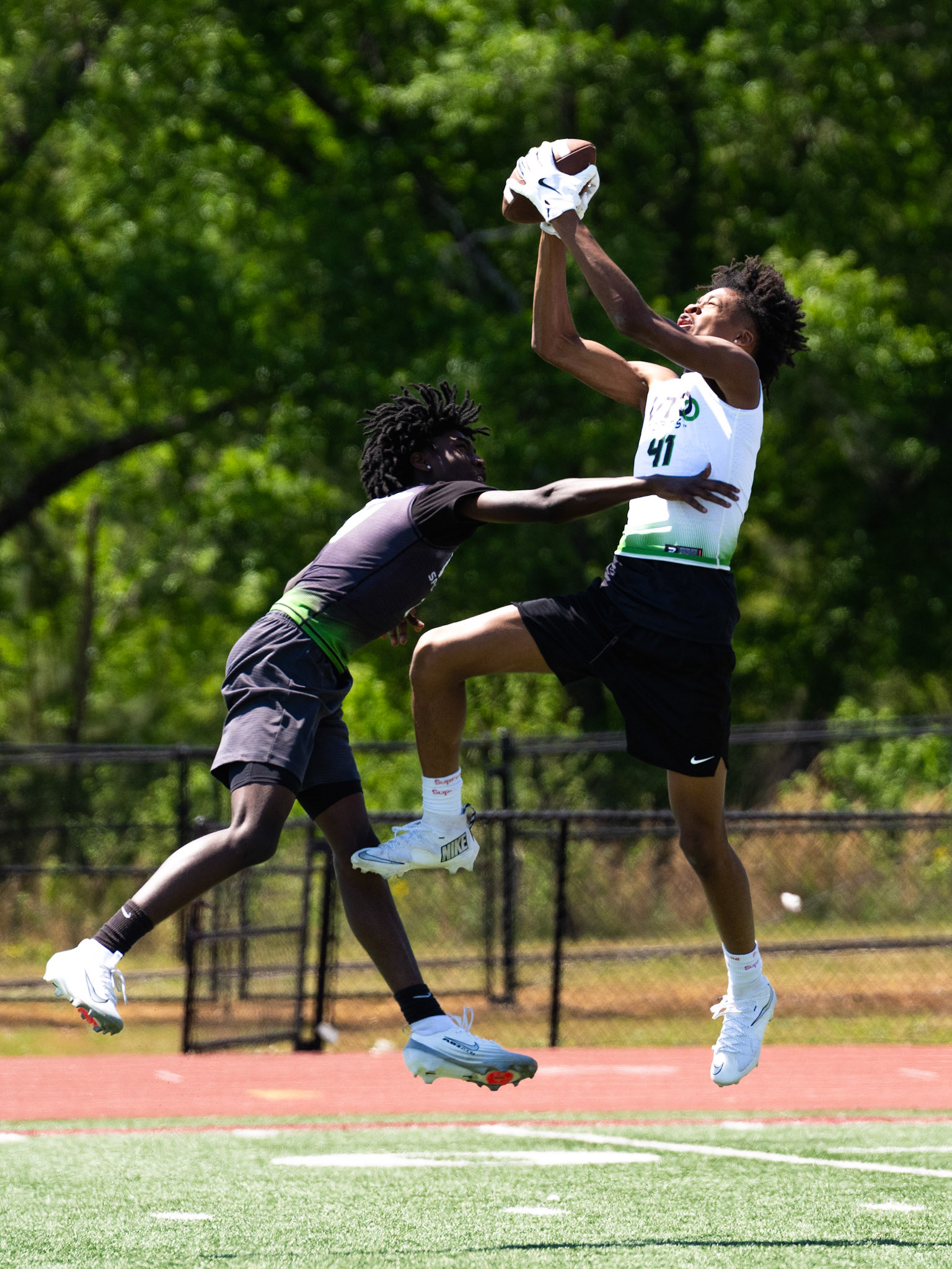 Elite middle school athletes compete during a 7-on-7 drill as a wide receiver makes a contested catch over a defender.