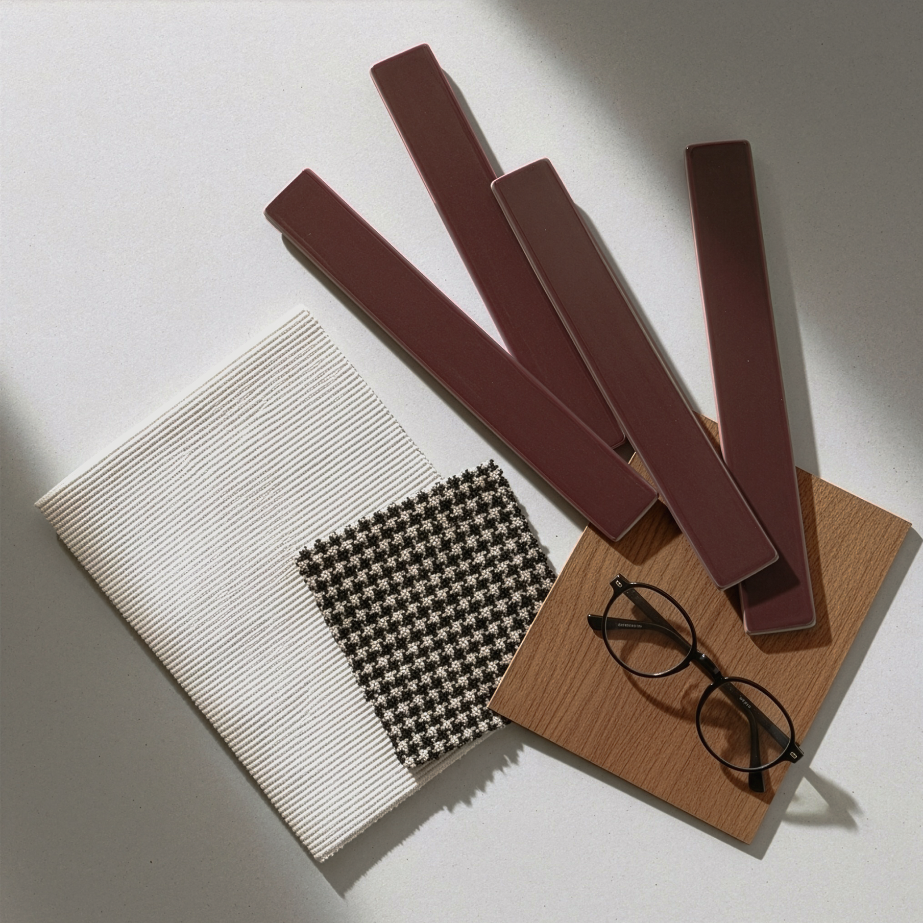A chic design mood board with maroon finger tiles, a classic houndstooth fabric swatch, and stylish eyeglasses.