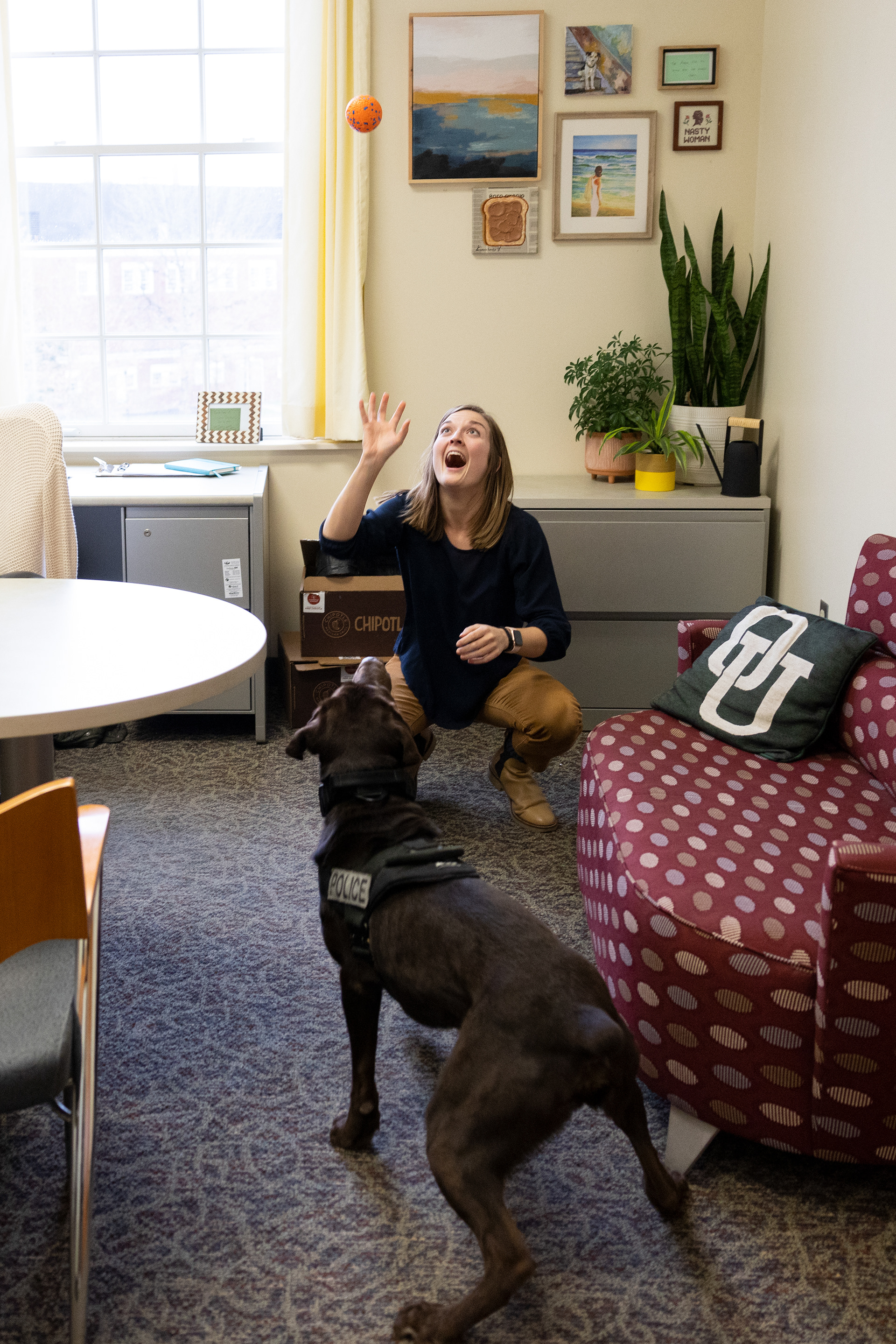 Mak Olaker, who works with the Dean of Students, throws a ball to Bach in Baker Center in Athens, Ohio, Nov. 20, 2023. She bought the ball on Amazon just for Bach. Her office is one of the usual stops that Officer King and Bach make on their walk around campus. “This is the third ball I’ve bought for Bach. The tennis ball lasted around 15 minutes. This ball is surviving fairly well,” Olaker said. Mak loves it when Bach comes to her office because it gives her a mental break and brightens up her day.