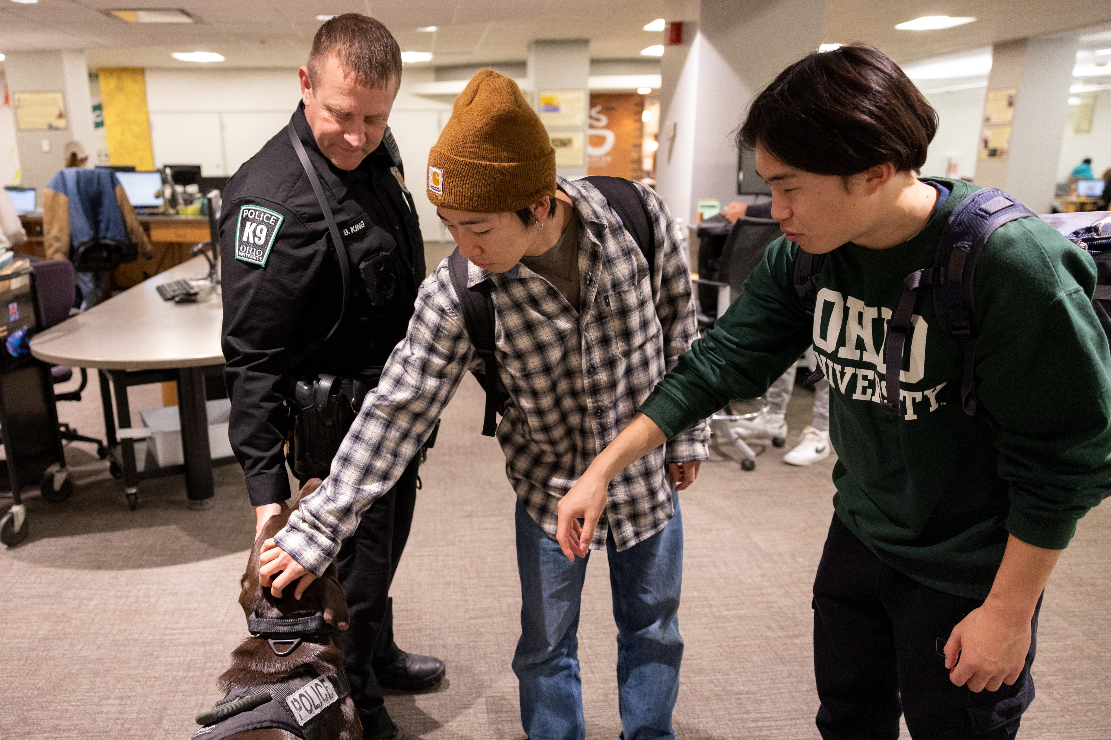 Two students pet Bach after asking permission from Officer King at Alden Library in Athens, Ohio, Nov. 20, 2023. Officer King and Bach are known by many students and faculty on campus. “He kinda acts like a therapy dog. A lot of these students haven’t seen their dogs in months, so they love petting Bach,” Officer King said. He tries to bring Bach around students to lower their stress and to also introduce himself. He wants students to know that the police aren’t people to worry about and that they are nice to talk to.