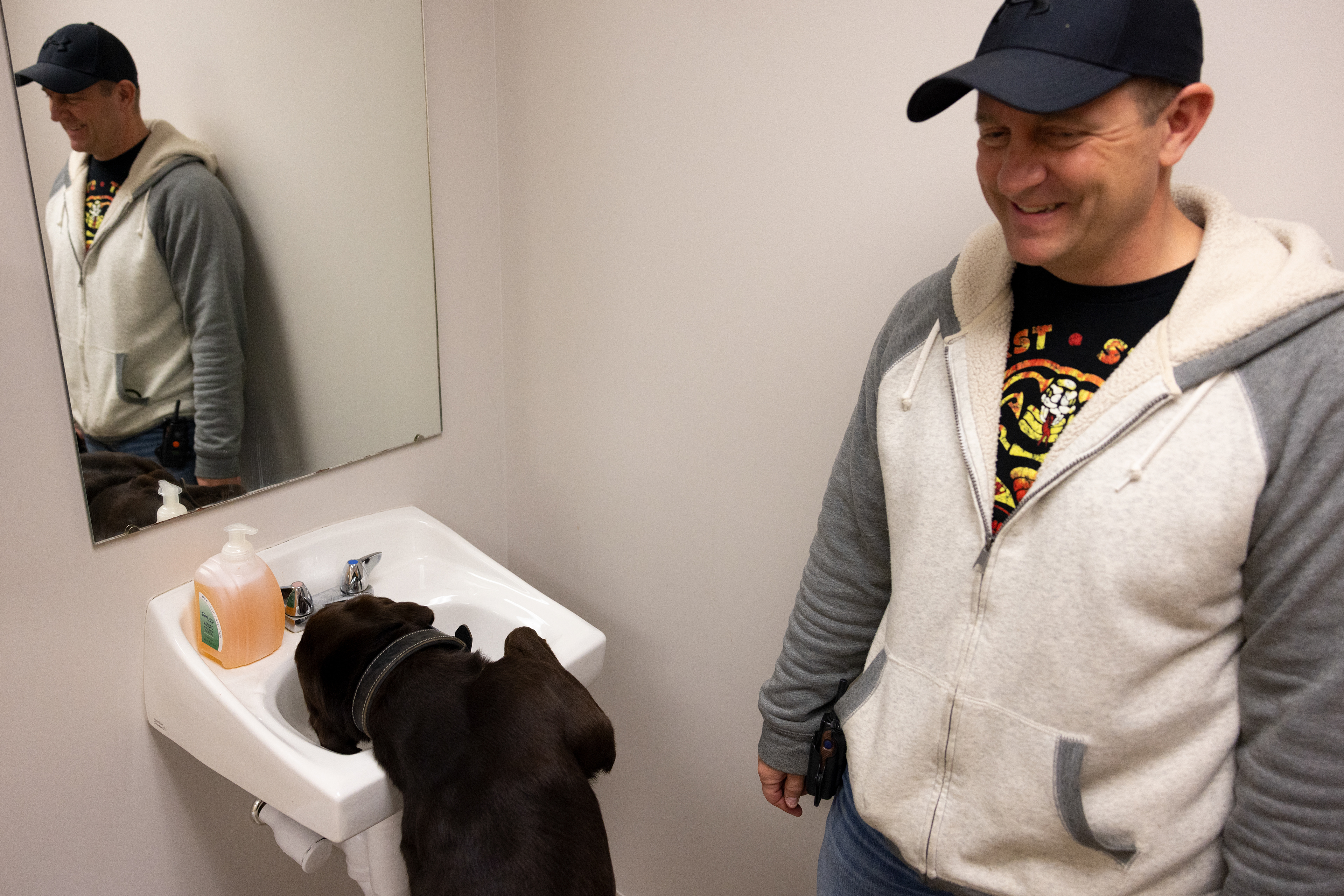 Officer King turns the facet on in the bathroom to let Bach have a drink at Christ Community Wesleyan Church in Athens County, Ohio, Dec. 2, 2023. He carries around a foldable bowl that he usually uses, but he finds this way to be more fun.