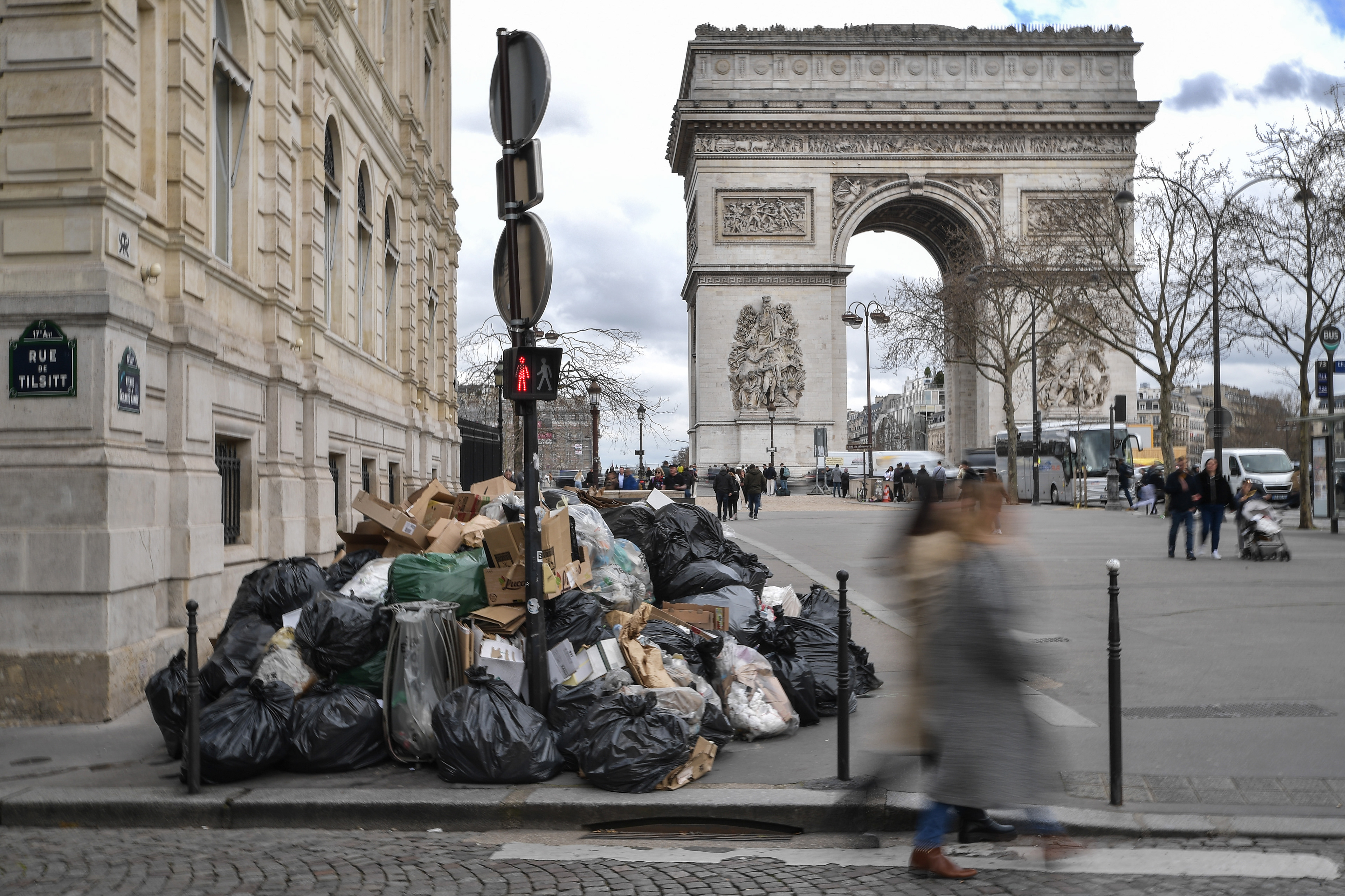 Pedestrians walk past accumulated garbage on the sidewalk in front of the Arc de Triomphe in Paris on March 21, 2023. Sanitation workers have been on strike since March 6, contesting the French government's bill to raise the legal retirement age from 62 to 64.
