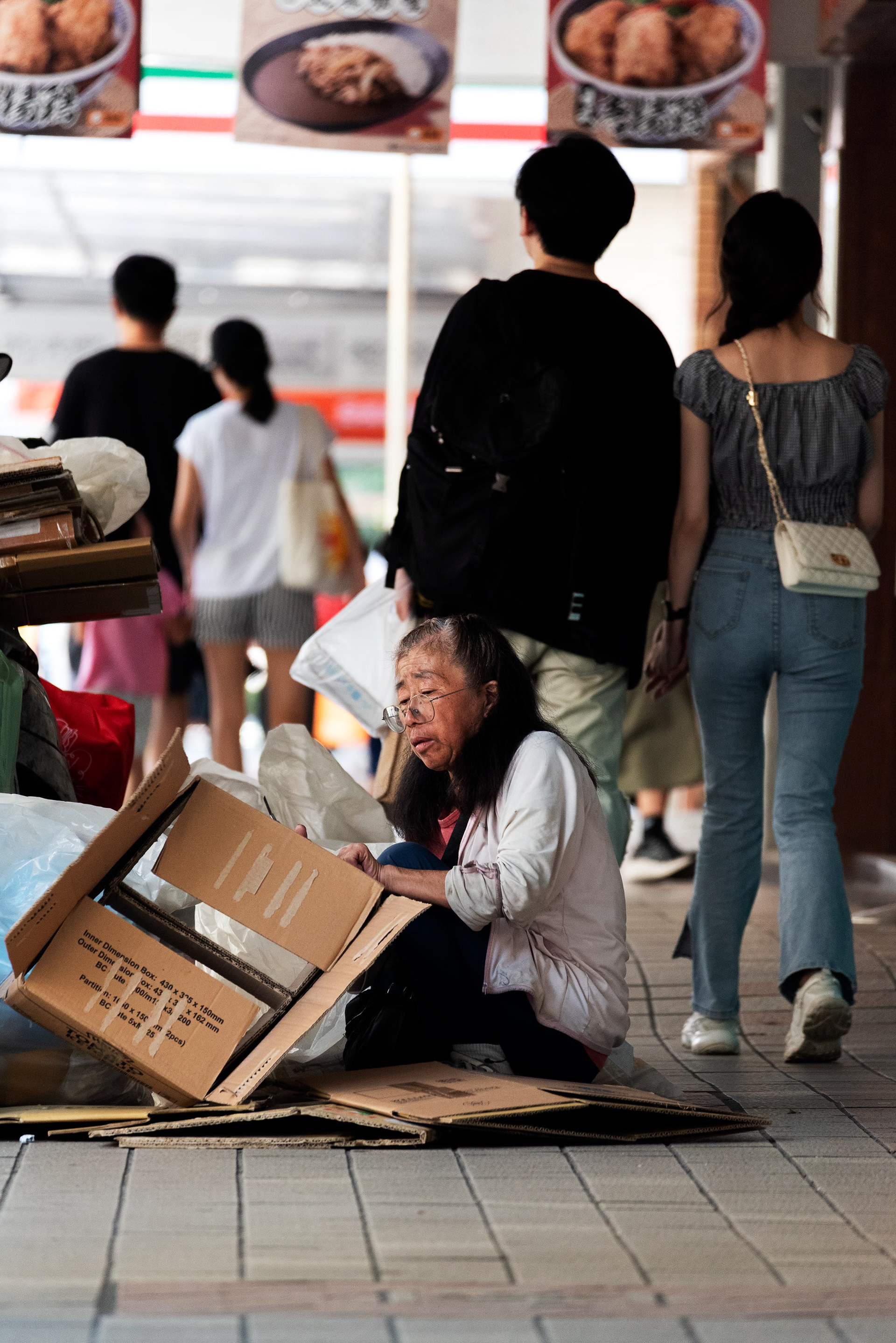 an elderly woman carefully arranges used cardboard, readying it for sale