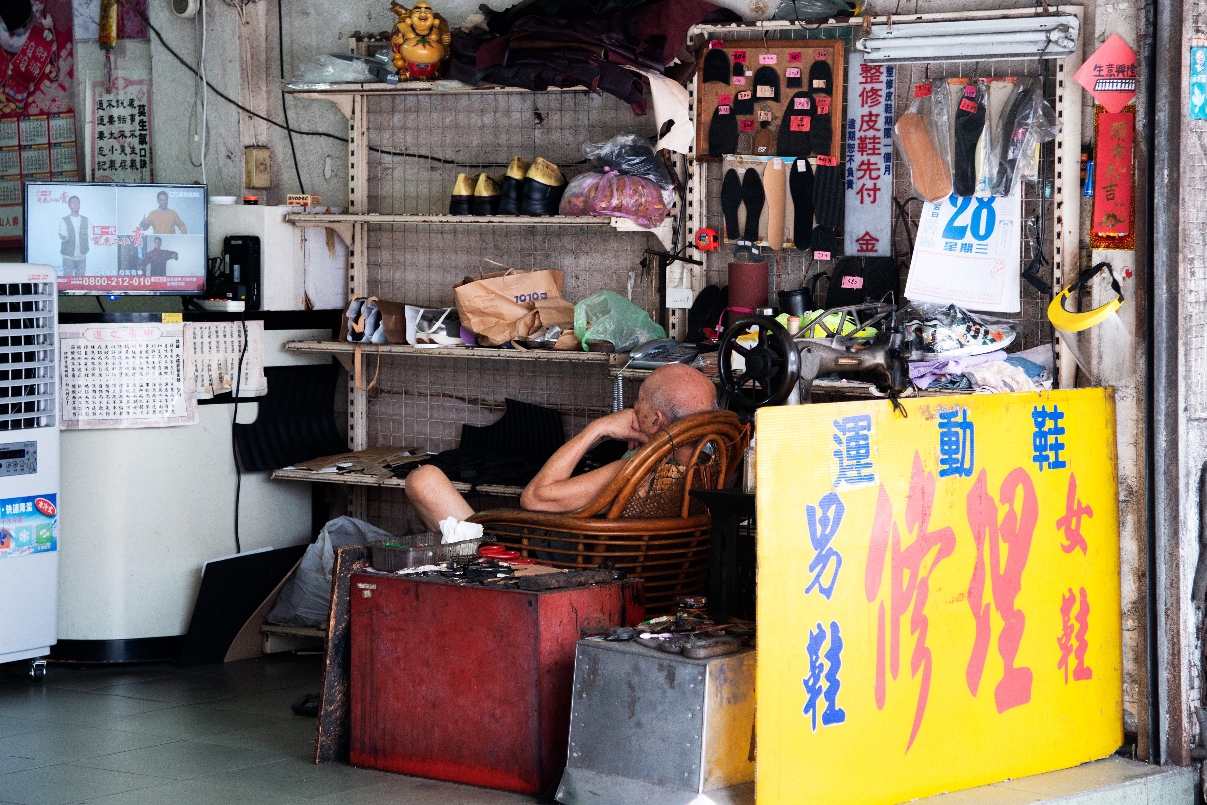in his small workshop, a cobbler rests quietly, eyes fixed on the television