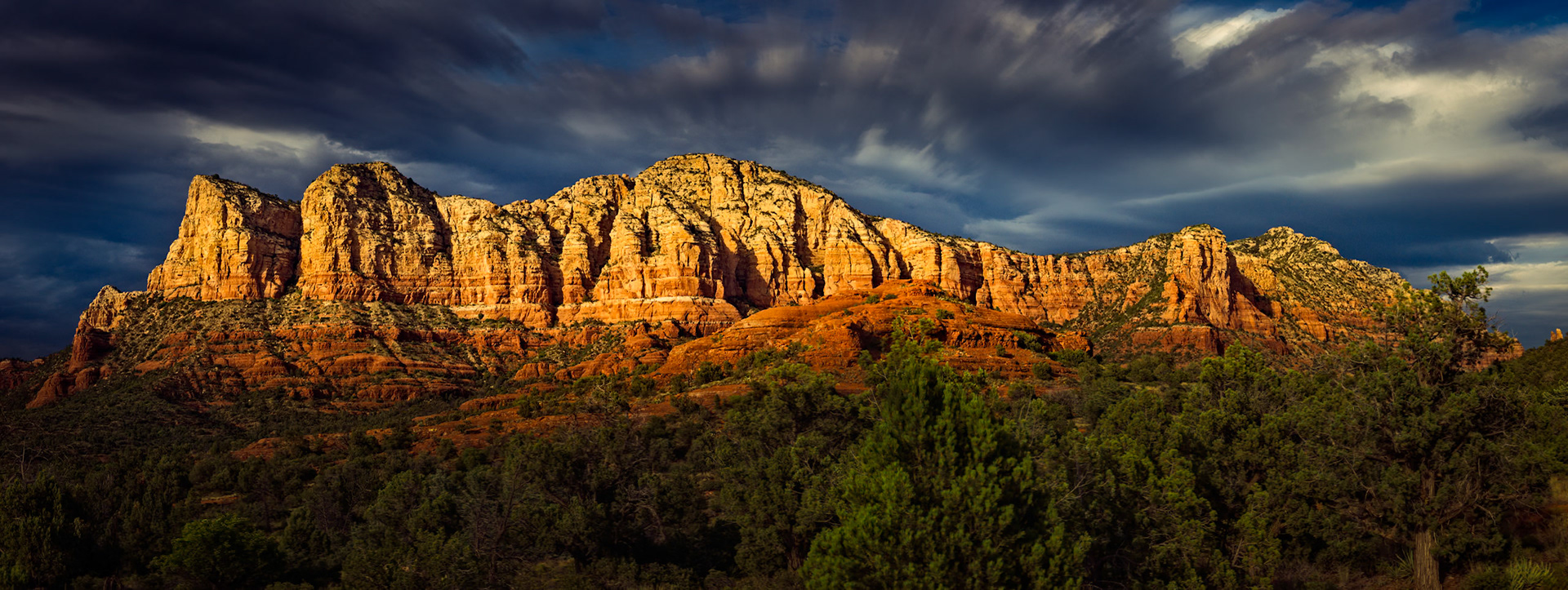 CATHEDRAL OF FIRE  |  Sedona has a way of making you feel small, but not insignificant. The towering red rock formations have stood through countless storms, seasons, and centuries, yet for a few fleeting moments they can be transformed by a single shaft of sunlight.As dark clouds swept overhead, the landscape seemed caught between two worlds. The storm brought drama and tension to the sky while the last warm light of day ignited the sandstone cliffs, turning them into glowing walls of gold and crimson. The contrast lasted only moments before the light shifted again.What drew me to this scene was not simply the beauty of Sedona, but the reminder that extraordinary moments often arrive between extremes. Between light and shadow. Between calm and storm. Between what is permanent and what vanishes in an instant.