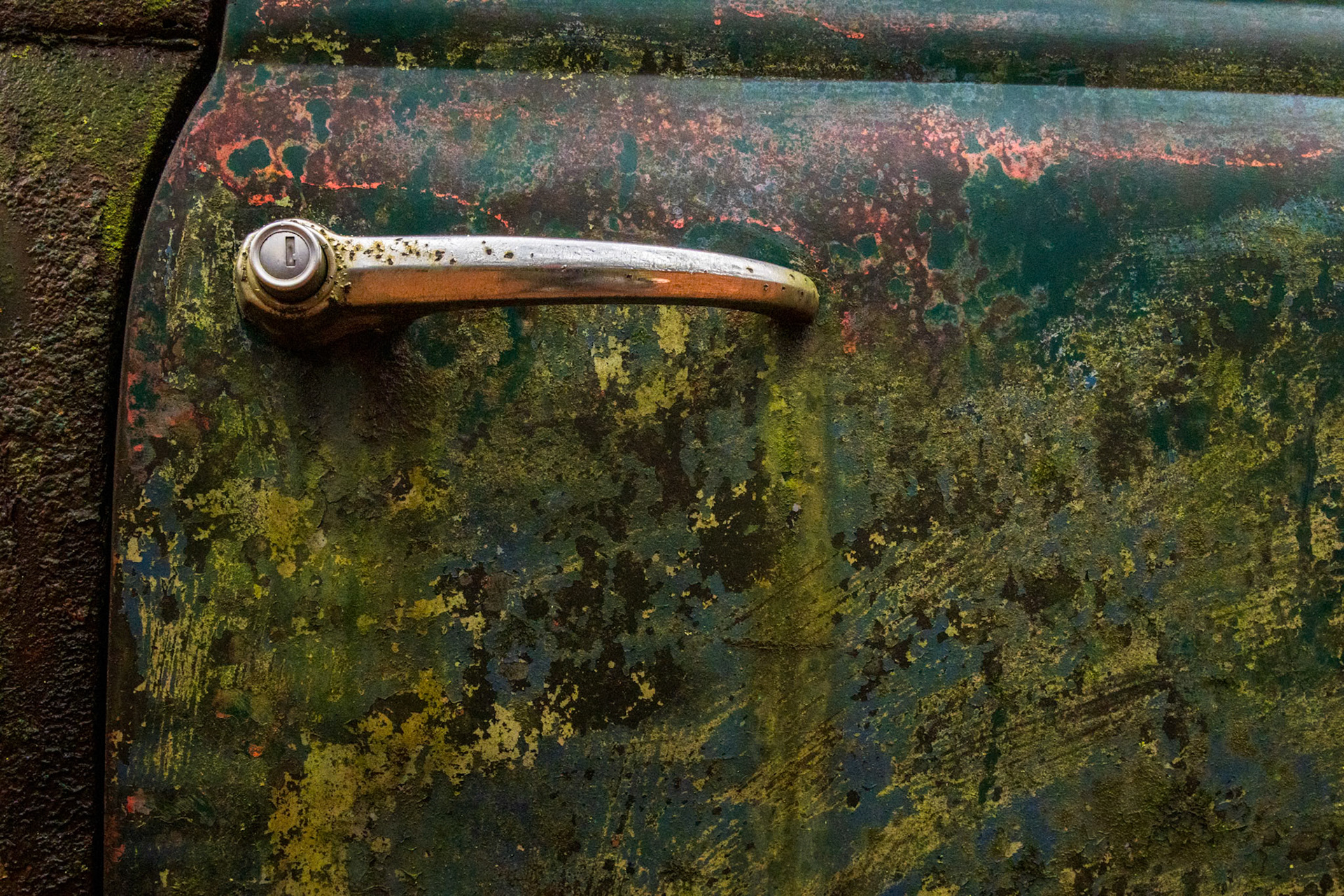 MOSS AND MEMORY  |  A simple door handle is all that remains of an invitation to a world long gone. Time has transformed painted steel into a rich tapestry of color and texture, where rust, lichen, and weather have created patterns no artist could deliberately reproduce. What was once functional has become unexpectedly beautiful.I am drawn to images like this because they ask a quiet question: would you still open the door? Though the vehicle itself has surrendered to time, the handle remains, waiting patiently as if someone might still arrive, turn the latch, and continue a journey that ended decades ago.