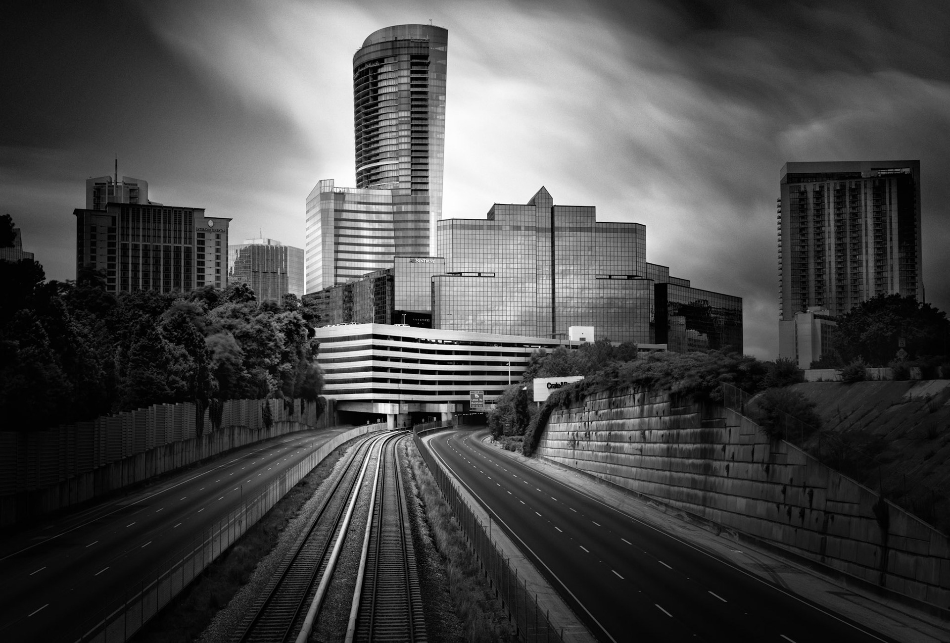 QUIET TRANSIT  |  Anyone who knows Atlanta knows this scene is impossible.The Downtown Connector is one of the busiest stretches of highway in the Southeast, carrying hundreds of thousands of vehicles every day. Traffic jams are expected. Empty lanes are not.Yet through the magic of a long exposure, the constant flow of cars vanished. What remained was something rarely seen: a silent corridor leading into the heart of the city. The railroad tracks and highway lanes become powerful leading lines, drawing the eye toward the skyline as if the city itself is pulling you forward.The absence of traffic transforms the image. What is normally chaotic becomes calm. What is usually defined by movement becomes still. The city appears to be holding its breath, suspended in a moment outside of time.The dramatic sky adds to the mood, with clouds streaking overhead while the buildings stand firm beneath them. Together they create a study in contrasts: motion and stillness, permanence and change, reality and illusion.Photography has the power to reveal scenes that never truly exist. For a few seconds, Atlanta became a place without traffic, a sight as remarkable as the skyline itself.