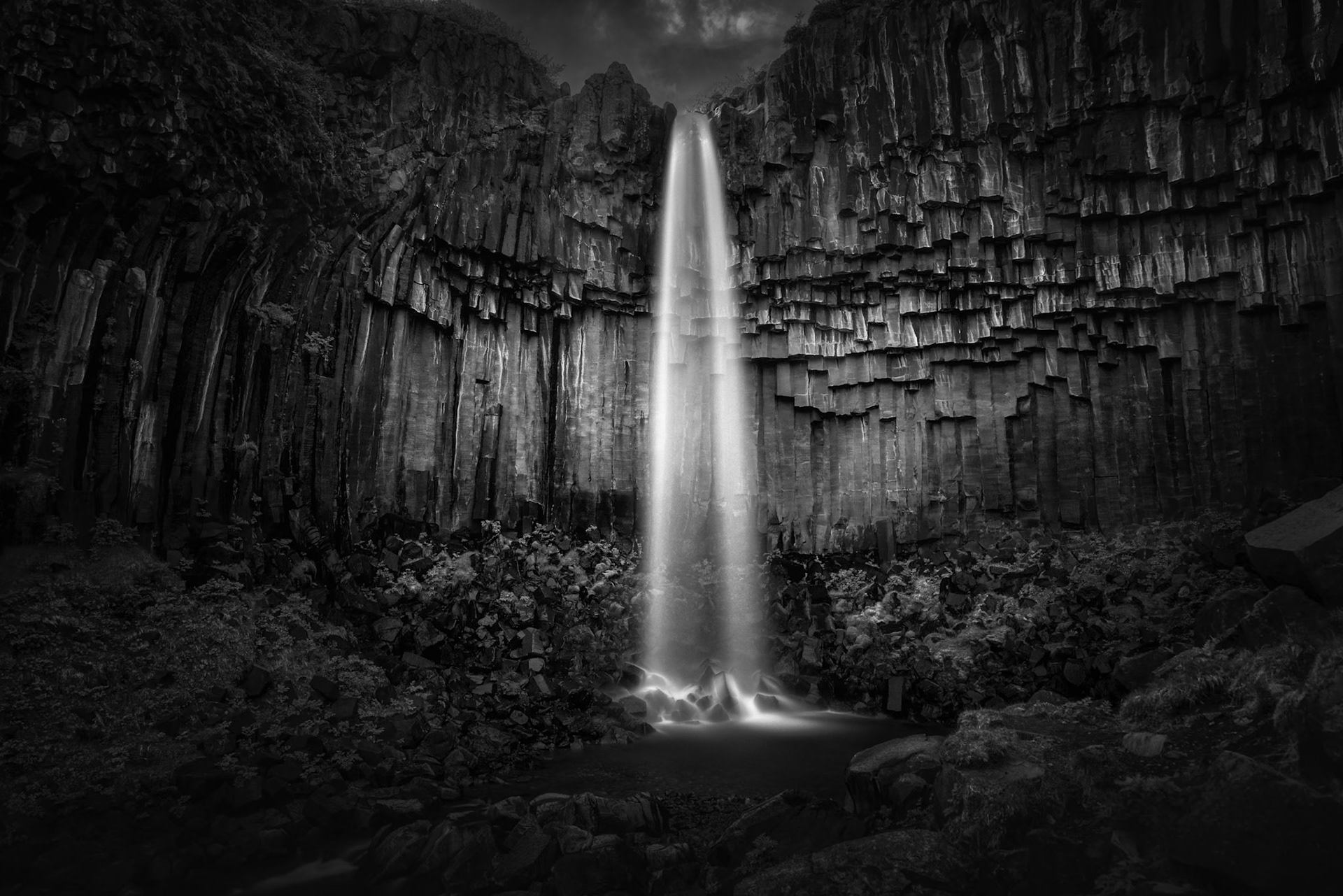 WHERE LIGHT FINDS STONE  |  Emerging from a fortress of ancient basalt columns, Svartifoss descends in a graceful ribbon of light through one of Iceland's most remarkable geological landscapes. The dark volcanic formations, sculpted by fire and time, create a natural cathedral that frames the waterfall with striking symmetry.