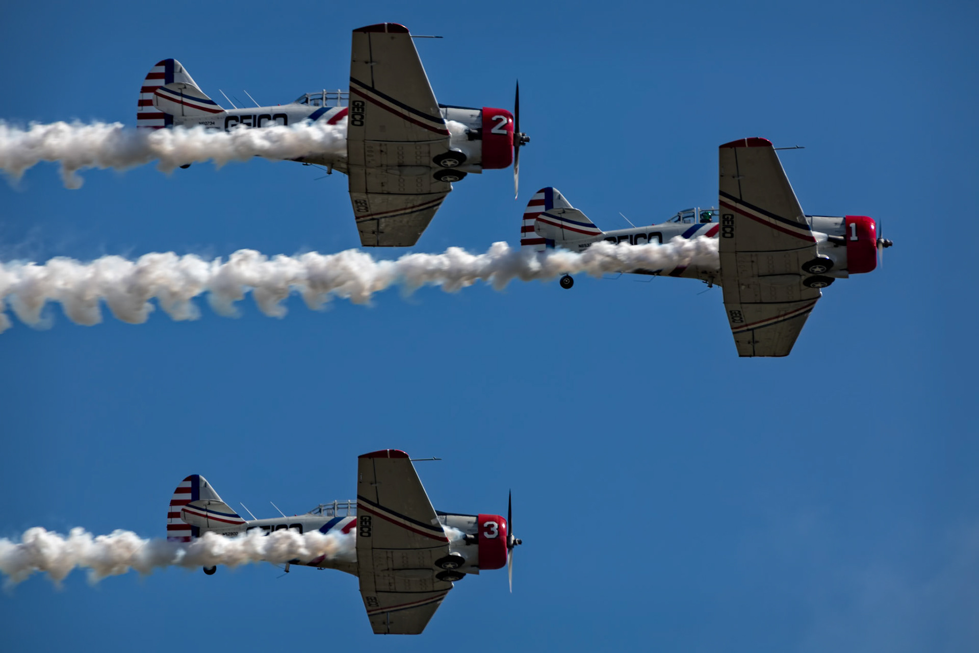 IN FORMATION  |  Against a cloudless sky, three vintage aircraft streak past in perfect formation, their smoke trails drawing parallel lines across the blue canvas above. The precision appears effortless, but every movement is the result of extraordinary skill, trust, and discipline.Airshow performances often last only a few minutes, yet they are built upon thousands of hours of training. Pilots fly separated by mere feet, relying on instinct, experience, and unwavering confidence in one another. In those moments, three individual aircraft become a single coordinated machine.