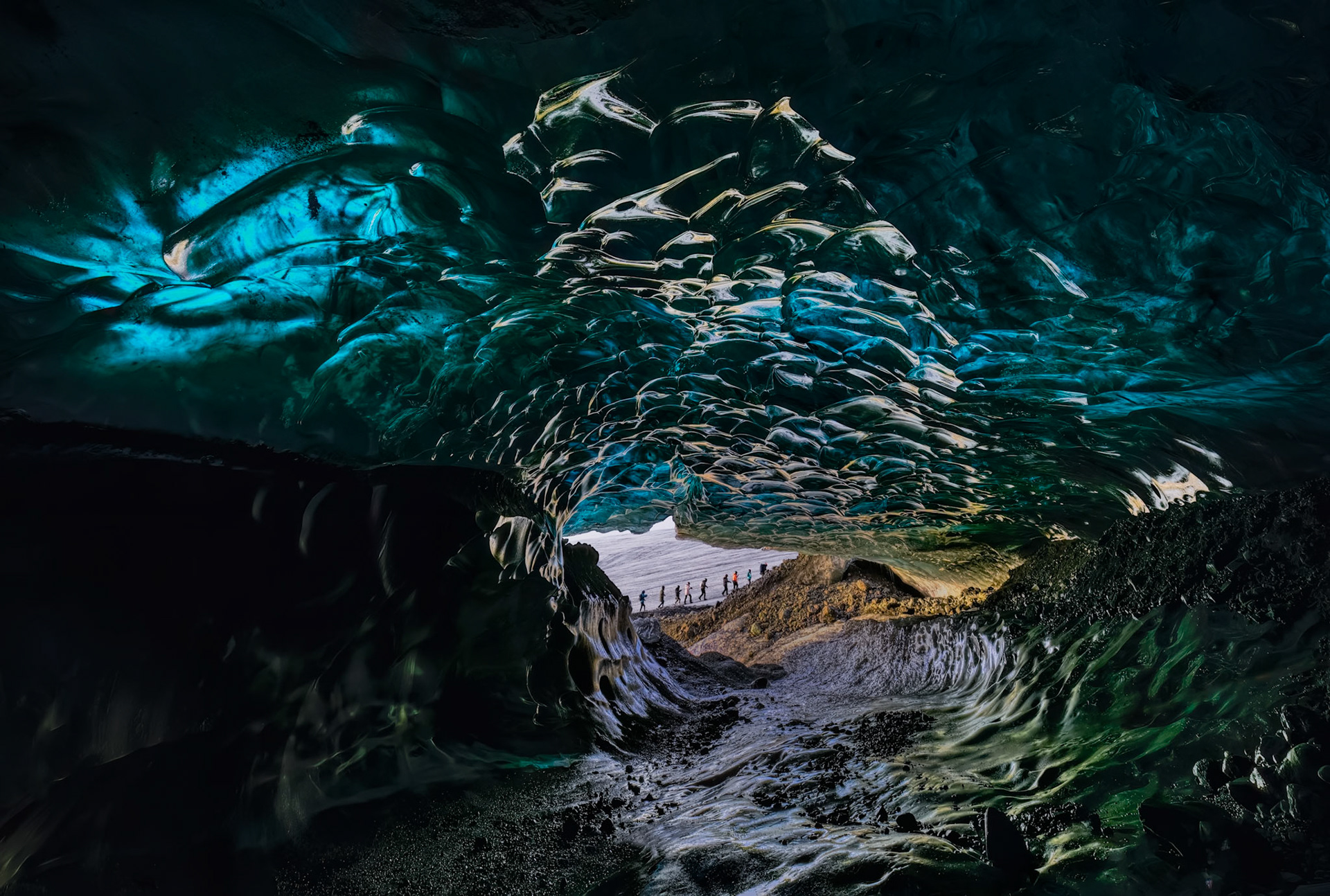 BENEATH THE BLUE VEIL  |  Hidden beneath one of Iceland's glaciers lies a world few people ever experience. Sculpted by meltwater and time, this ice cave glows with shades of blue, turquoise, and emerald, transforming ancient ice into something that feels more like a natural cathedral than a geological formation.What fascinated me most was the ceiling. Layer upon layer of compressed glacier ice formed intricate patterns that resembled crystal, stained glass, or frozen waves suspended overhead. Every surface reflected and refracted light differently, creating an ever changing display of color and texture.The small figures near the cave's entrance provide a sense of scale. What appears at first to be an intimate space is actually immense, carved within ice that may have fallen as snow hundreds or even thousands of years ago. Standing inside was both exhilarating and humbling, a reminder that some of nature's most extraordinary creations exist only briefly before melting away.