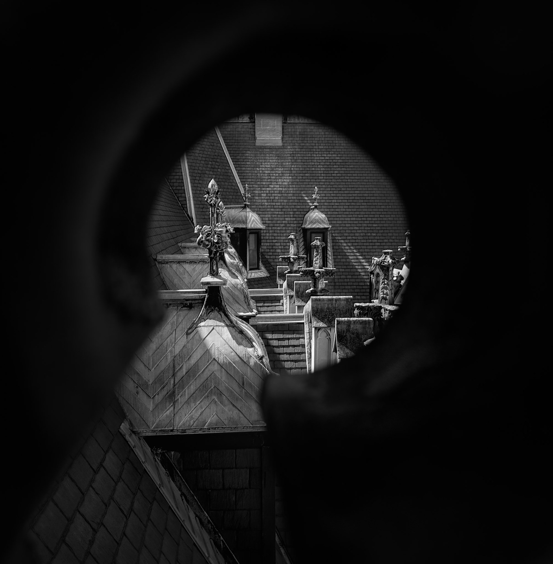 THROUGH THE KEYHOLE  |  A narrow opening reveals a hidden view of the Biltmore Estate's rooftops and architectural details. Framed by darkness, the eye is drawn through the opening to a scene that many visitors never notice.The image plays with curiosity and discovery, using the surrounding shadow to isolate the intricate stonework, chimneys, and decorative elements beyond. By limiting what can be seen, the composition encourages a closer look at the craftsmanship and complexity of the estate's design.