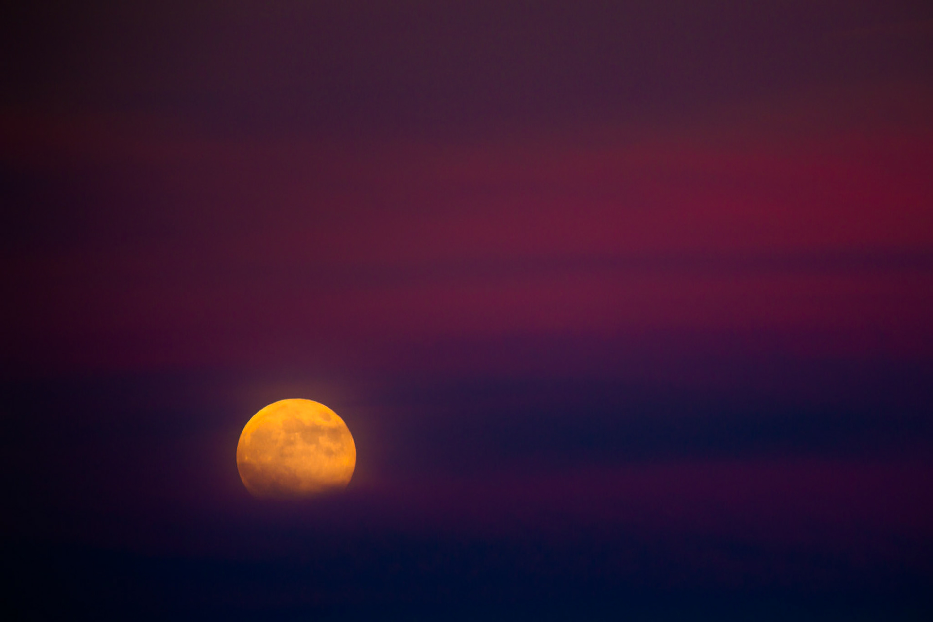 VEIL OF NIGHT  |  Night settles softly over the Caribbean as the ship glides toward the Panama Canal. Above the dark horizon, a full moon rises through layers of tropical haze, its golden glow muted by bands of violet and crimson cloud.There is a peculiar stillness at sea after sunset. Engines hum beneath the deck, distant lights flicker along the shoreline, and passengers gather quietly at the railings, watching the sky rather than speaking. The moon becomes a silent companion, keeping pace with the vessel as it moves toward one of the world's great engineering crossroads.